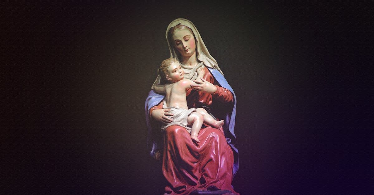 Statue of the Madonna holding baby Jesus, painted in pink and blue against a dark background