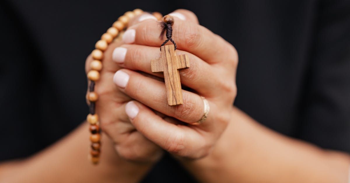 Hands holding a wooden rosary with a cross pendant against a dark background