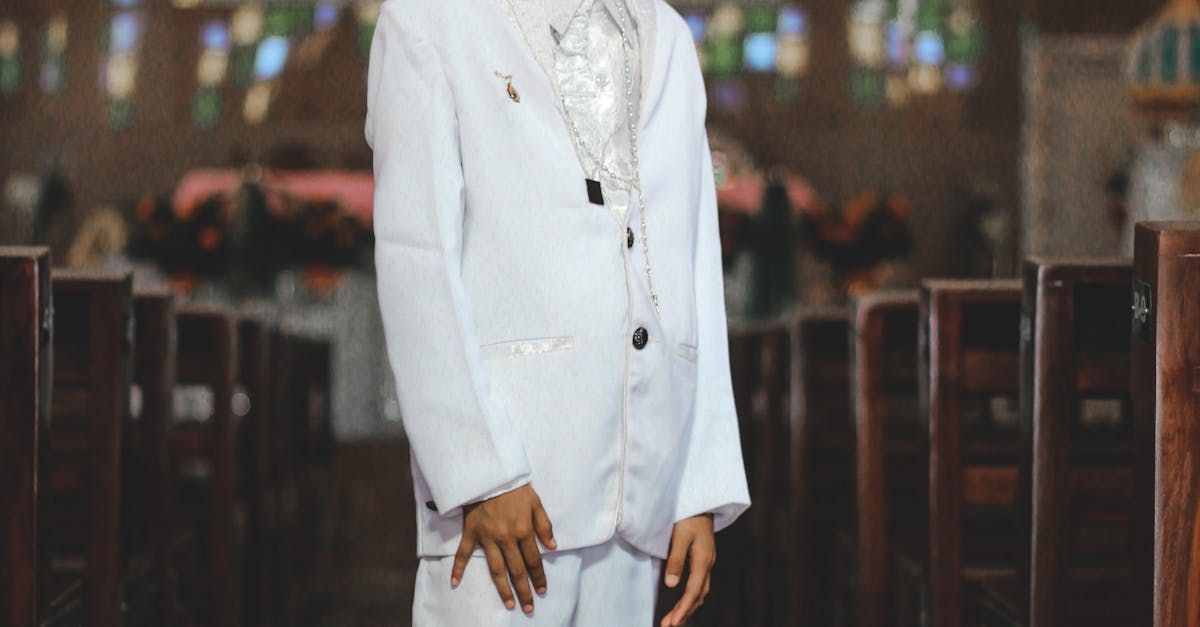 Person in a white suit standing inside a church with stained glass windows in the background