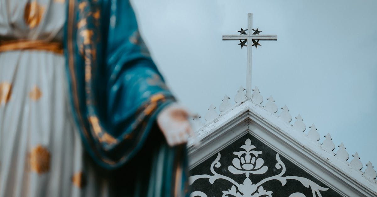 Cross atop a church roof, with a blurred blue-robed statue in the foreground