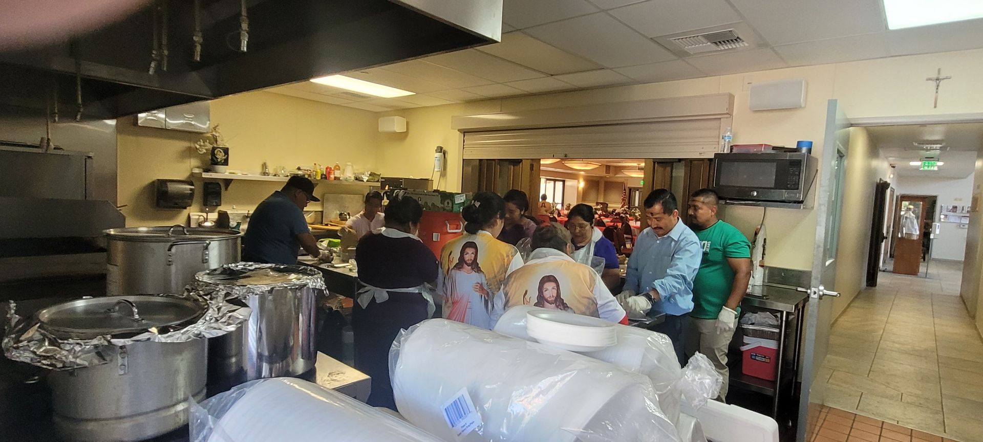 Crowded kitchen with people preparing food around large pots and supplies