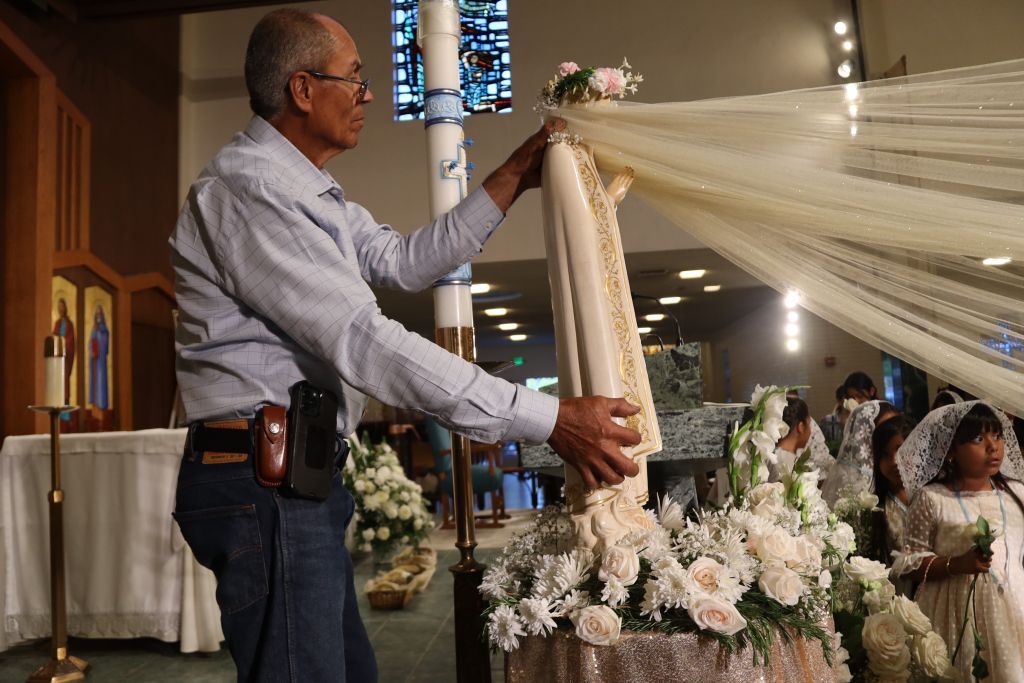 Man in a light blue shirt arranging a cream-colored net ribbon at a church ceremony
