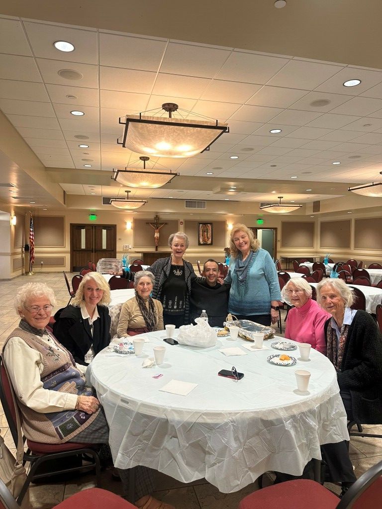 Group gathered around a white tablecloth table at a banquet hall, smiling and posing for a photo.