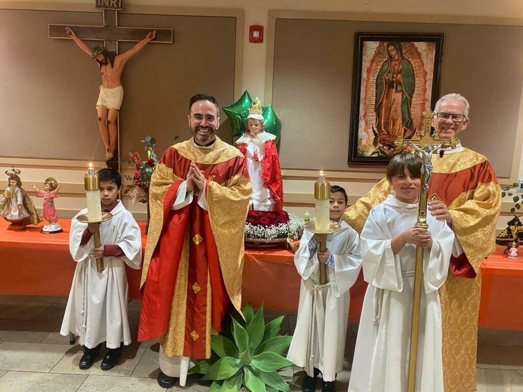 Clergy and altar servers standing in a church, two priests in red and gold vestments holding liturgical items