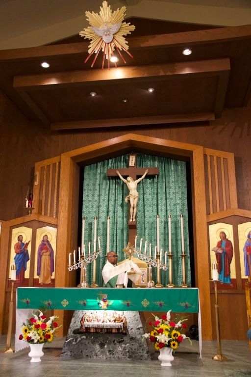 Church altar with crucifix, green backdrop, candles, flowers, and religious icons in a wooden sanctuary