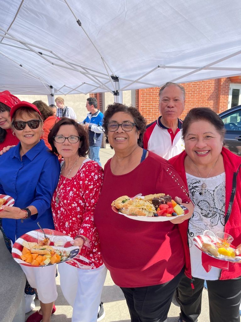 Group of people smiling and holding plates of food under a tent at an outdoor event