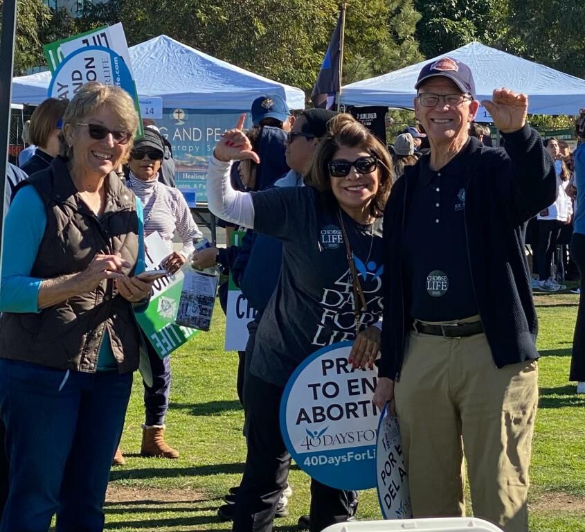 Three smiling people at a rally holding a sign reading “Right to End Abortion Ban”