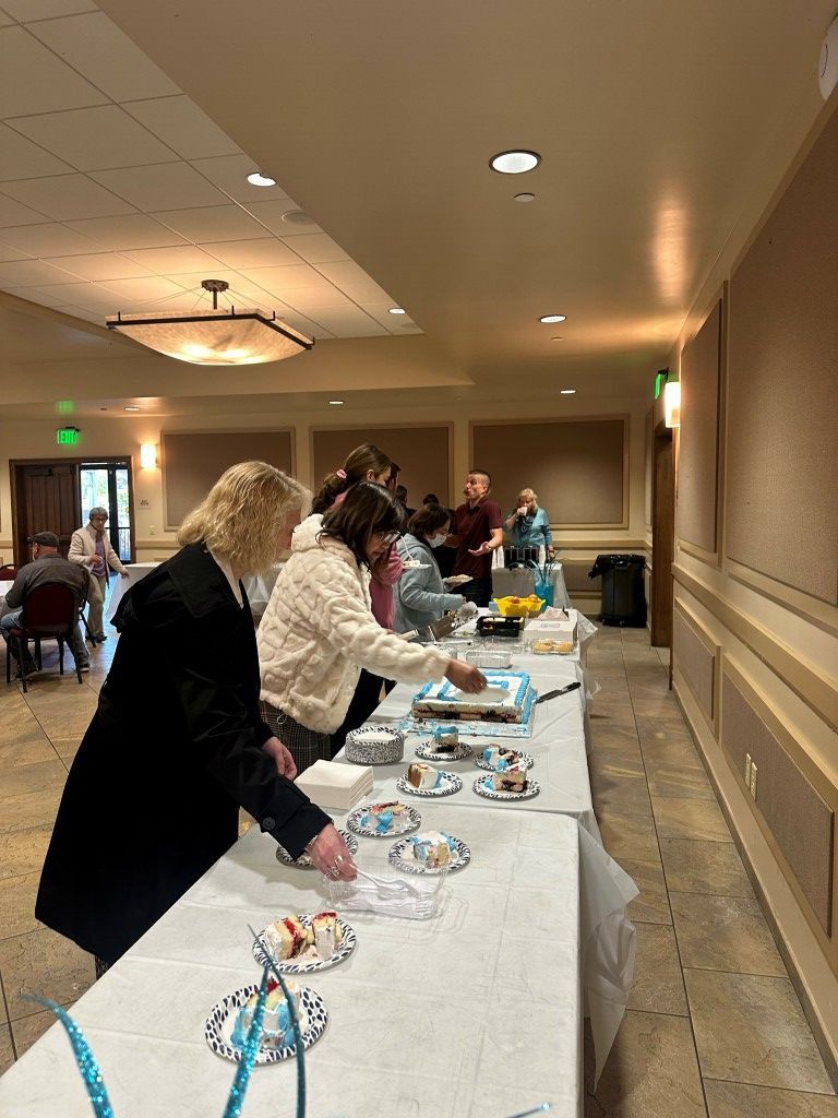 People serving food at a banquet table in a hallway, with trays and plates set out on white tablecloths