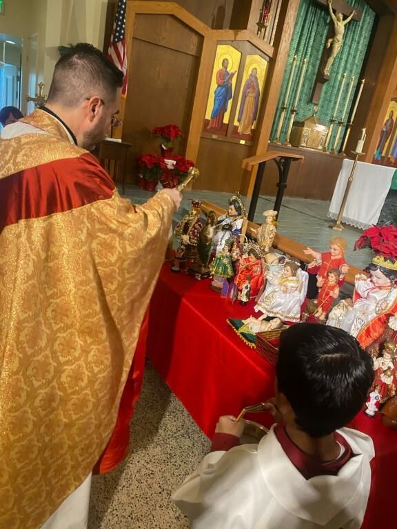Priest in gold robe blessing altar with red cloth and religious statues in a church