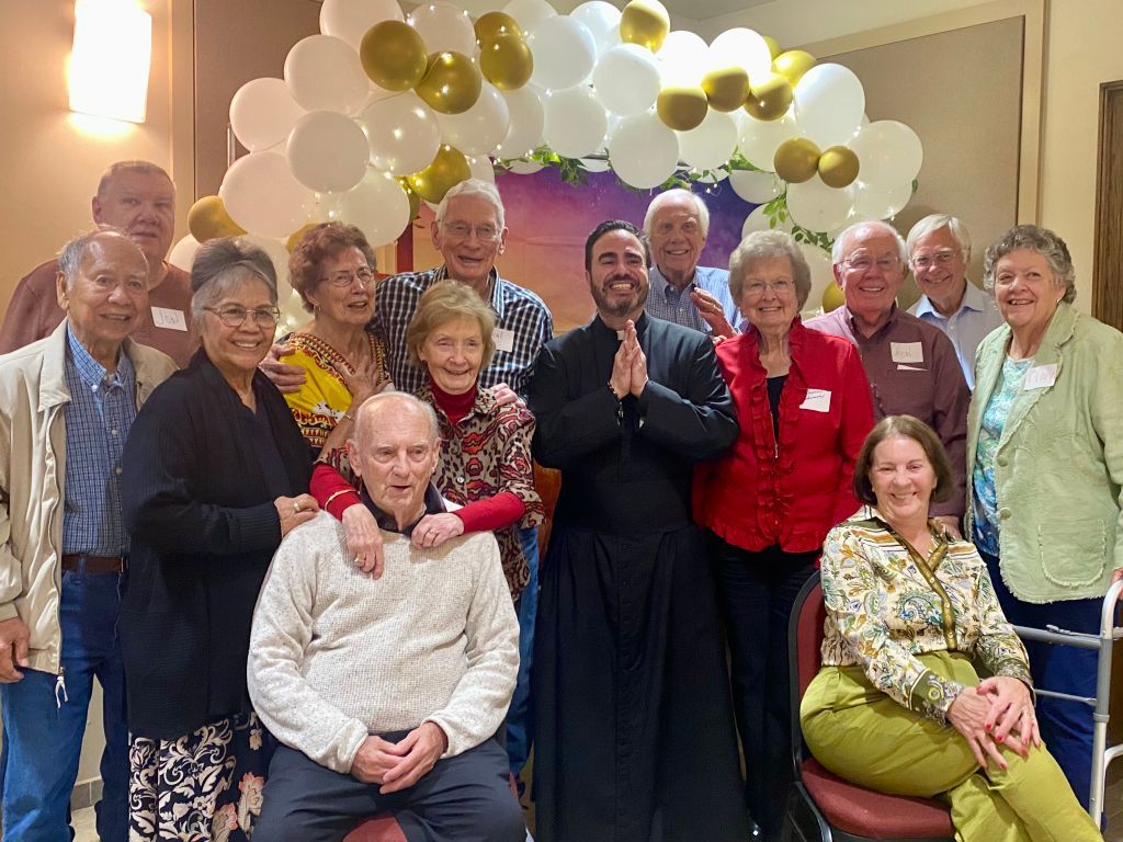 Group posing indoors in front of white, gold, and black balloons, celebrating together.