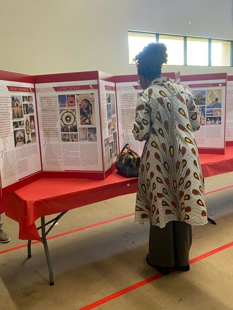 Person reading a poster display at a red-draped table in a bright room.