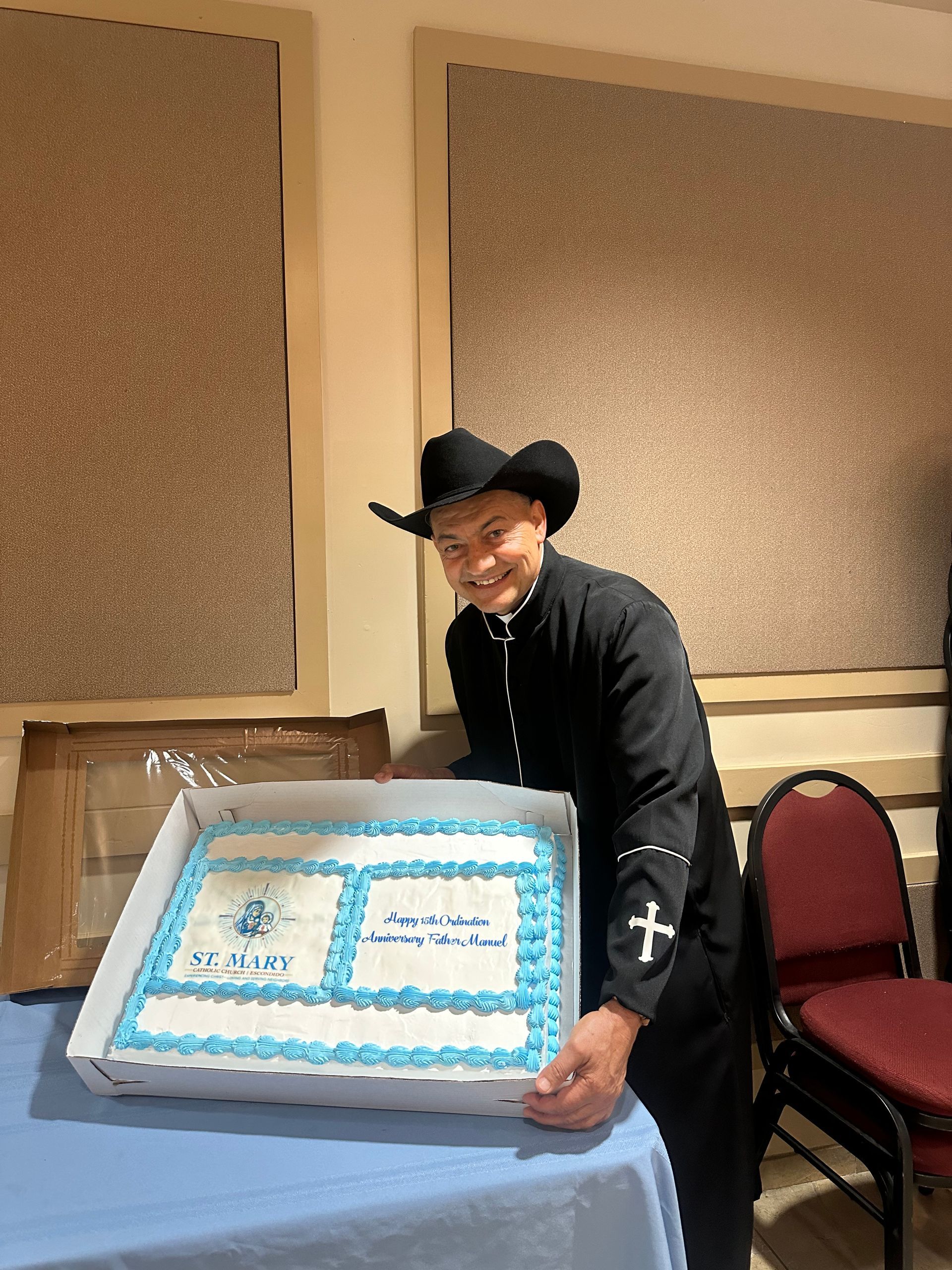 A person in a cowboy hat cuts a large blue-and-white sheet cake at a banquet table.
