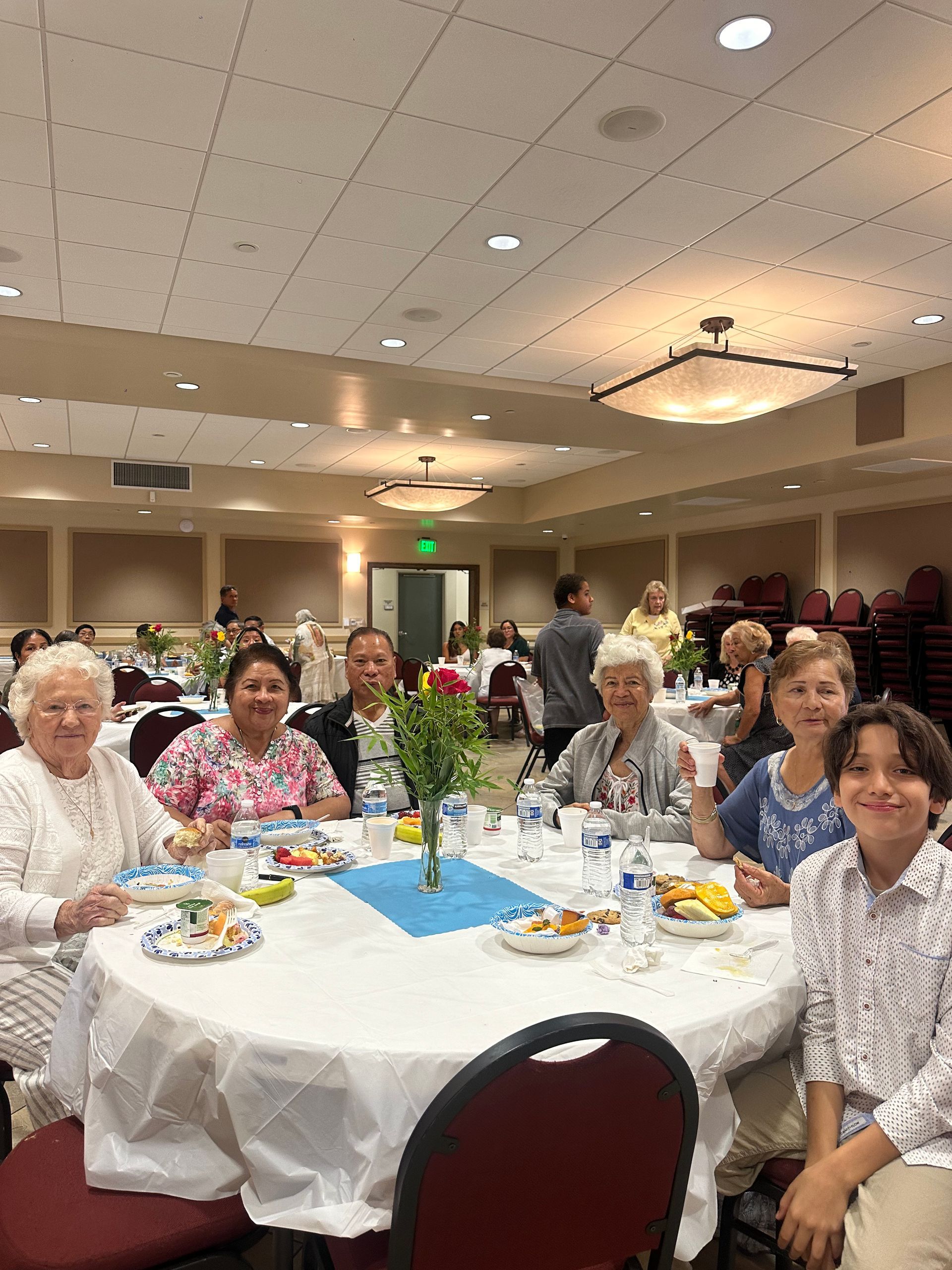 People seated at round tables in a banquet hall, sharing a meal and smiling toward the camera.