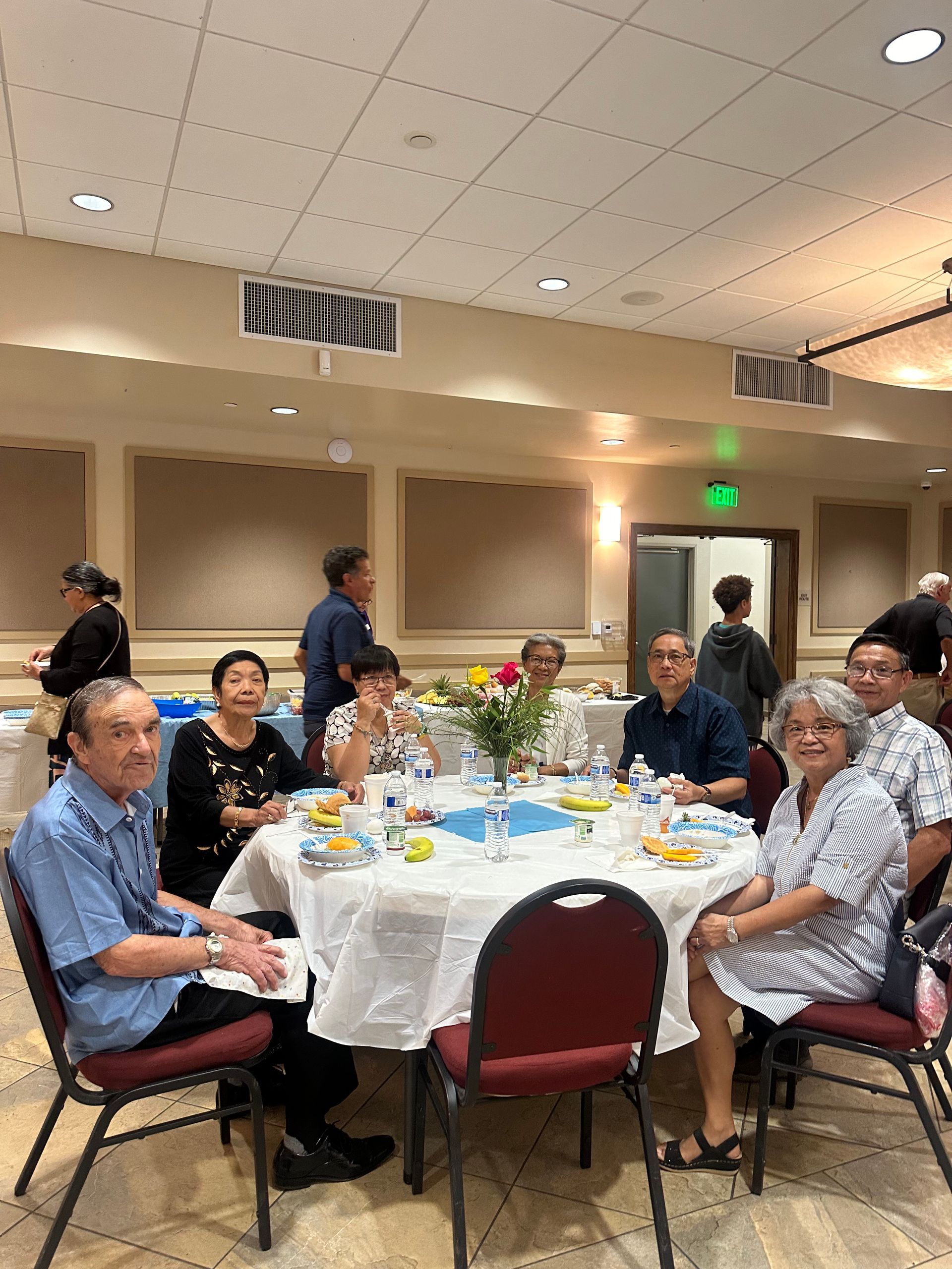People seated around a round table at an indoor community gathering.