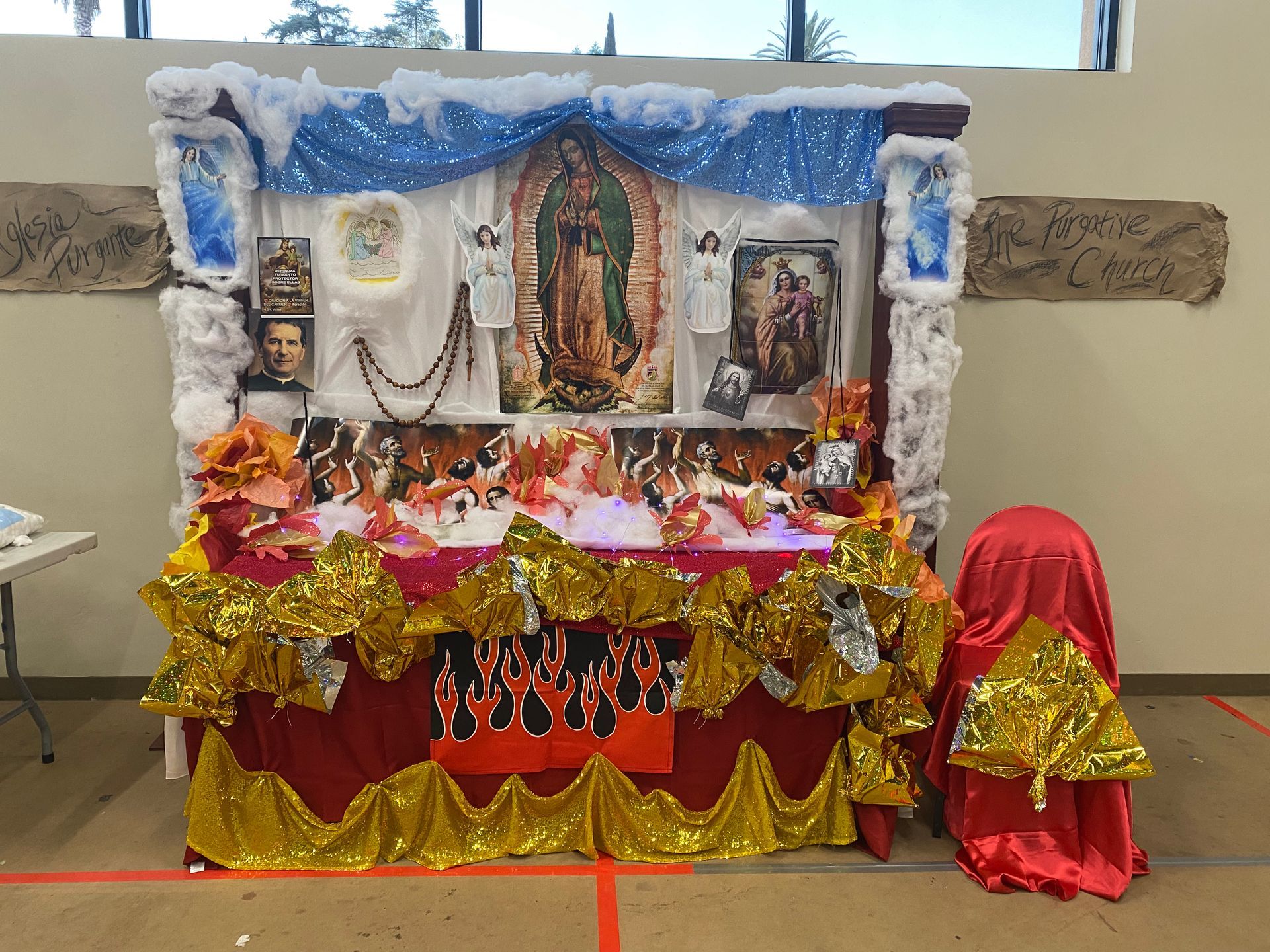 Decorated home altar with framed religious images, flowers, and red-gold fabric drapes