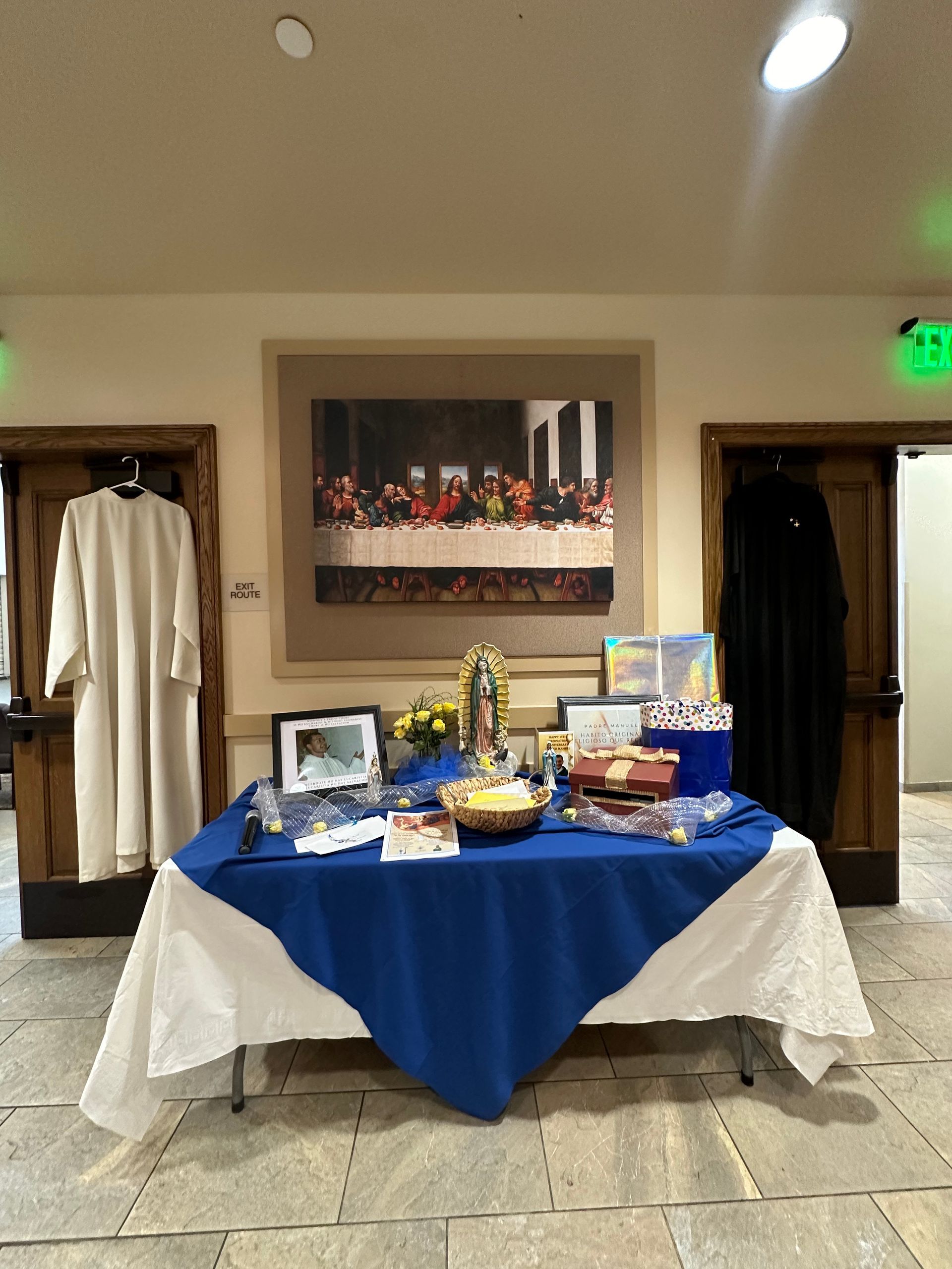 Refreshment table with blue tablecloth and assorted snacks in a hallway, flanked by hanging robes and framed artwork.