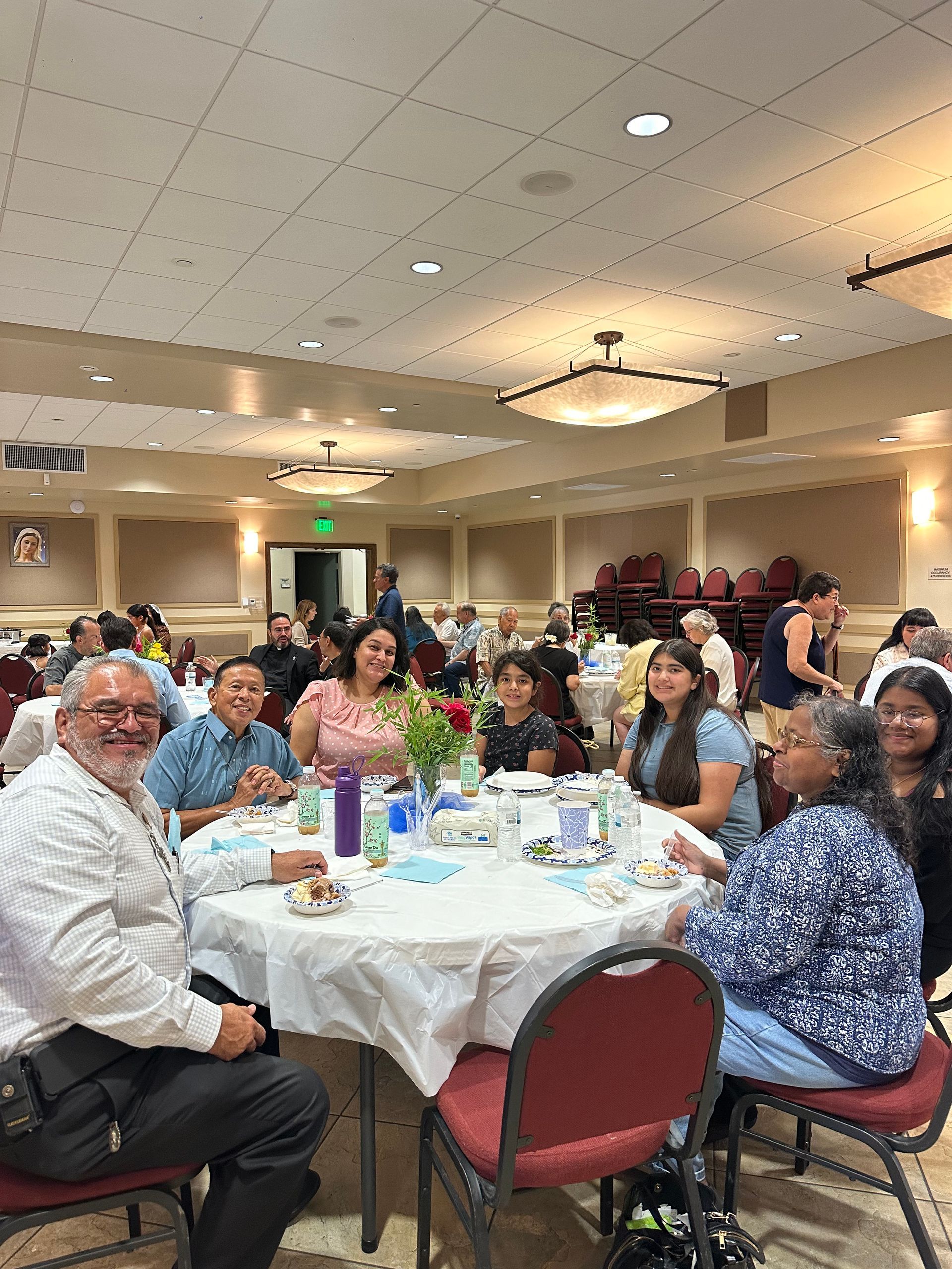 Banquet hall gathering with people seated at round tables, chatting under warm ceiling lights
