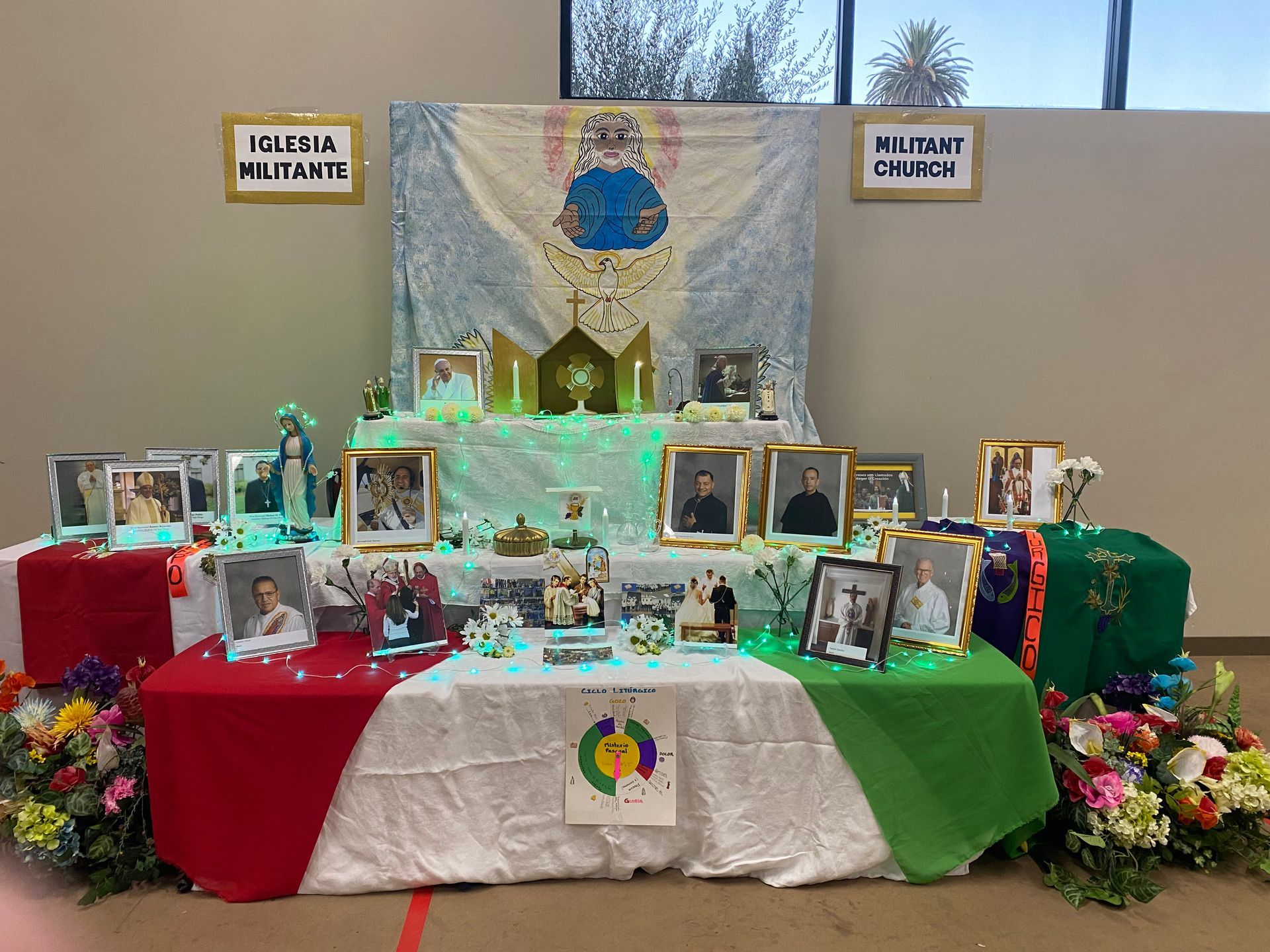 Decorated memorial display table with framed photos, candles, flowers, and red, white, and green cloths