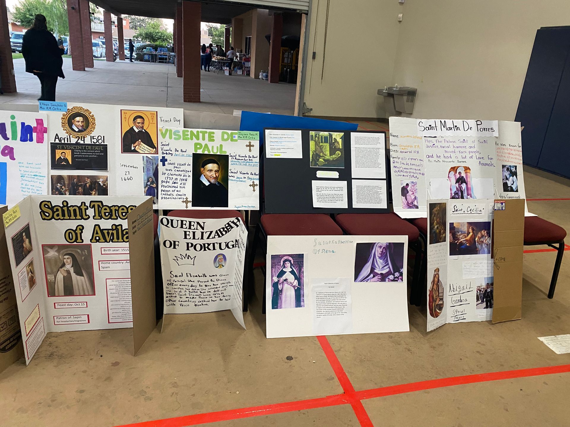 Science fair display boards arranged on the floor in a covered outdoor area, with posters, photos, and text.