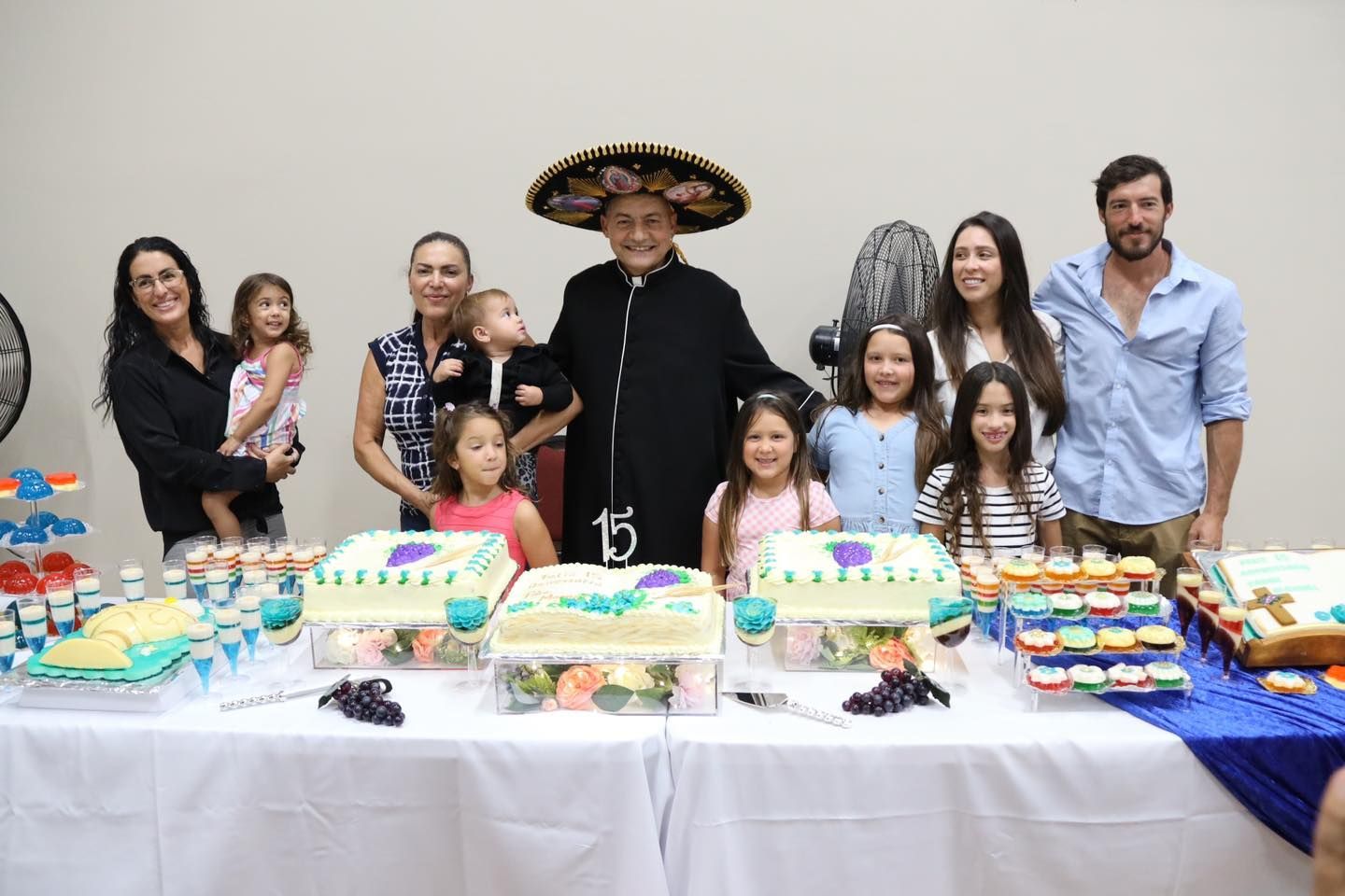 Group posing behind a birthday dessert table with colorful treats and a man in a sombrero at center