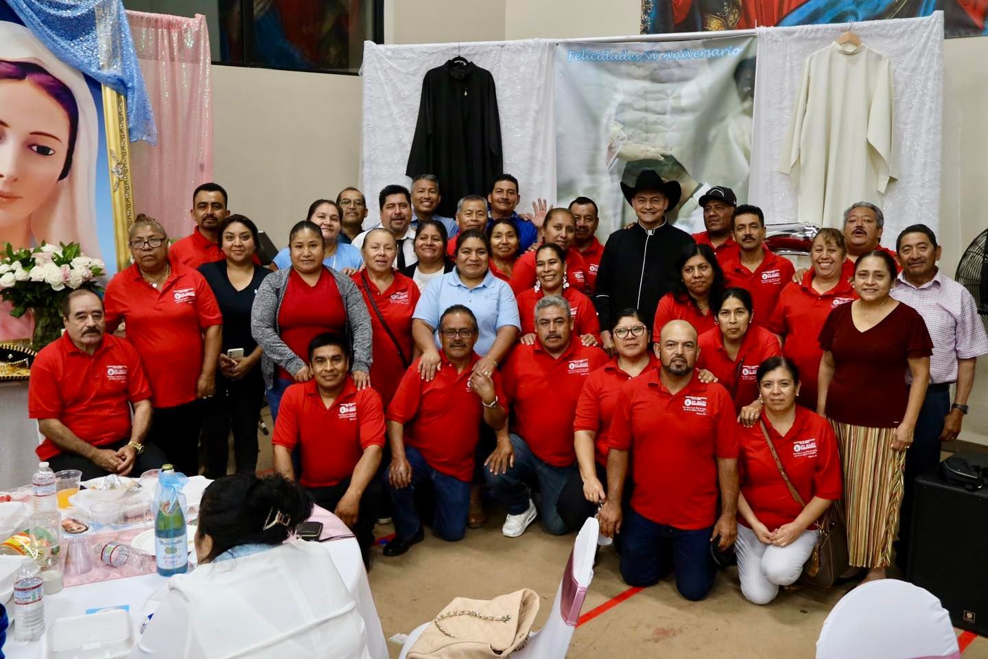 Group of people in red shirts posing at an indoor event booth with draped fabric backdrop