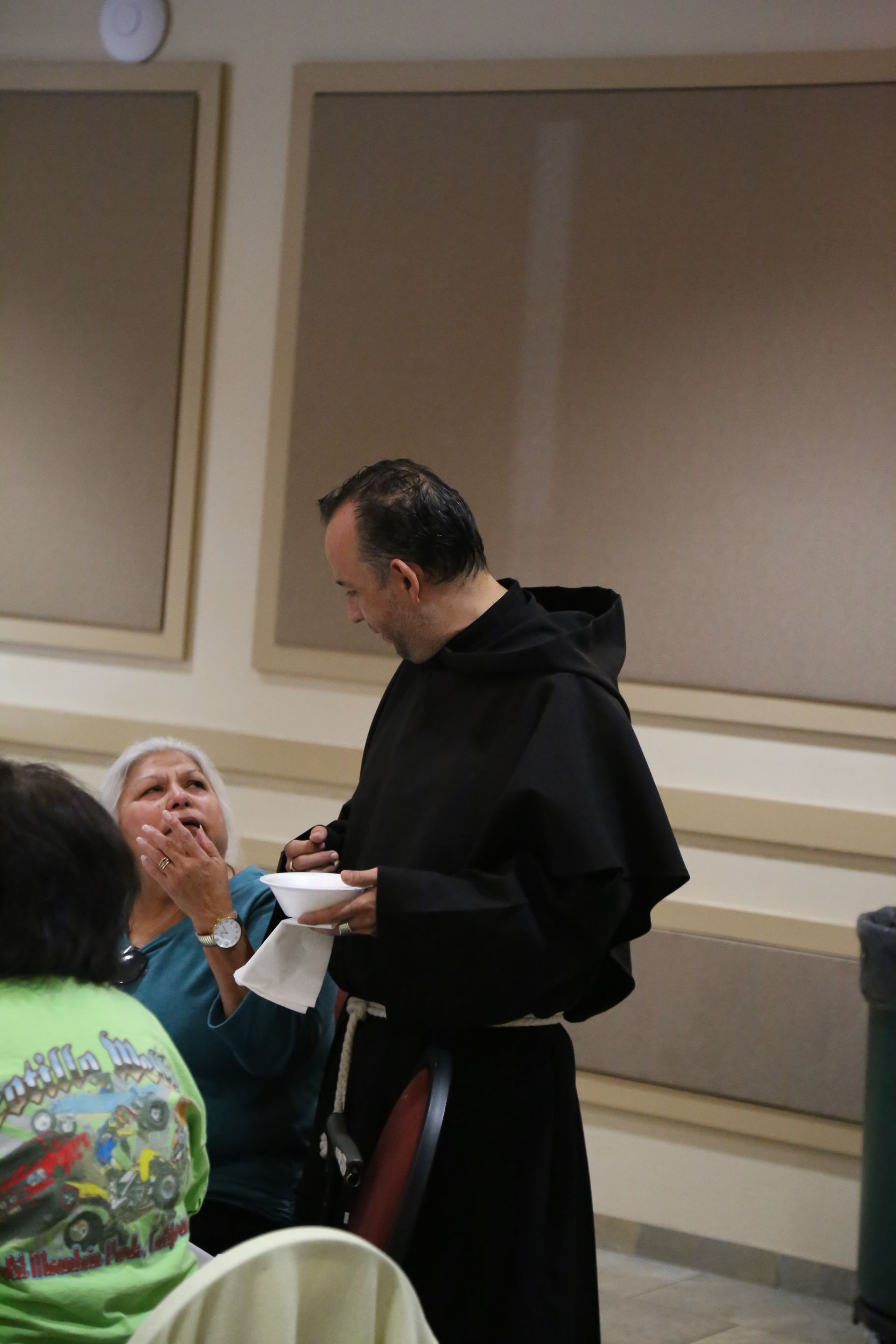 Man in a black robe speaks with seated women in a conference room