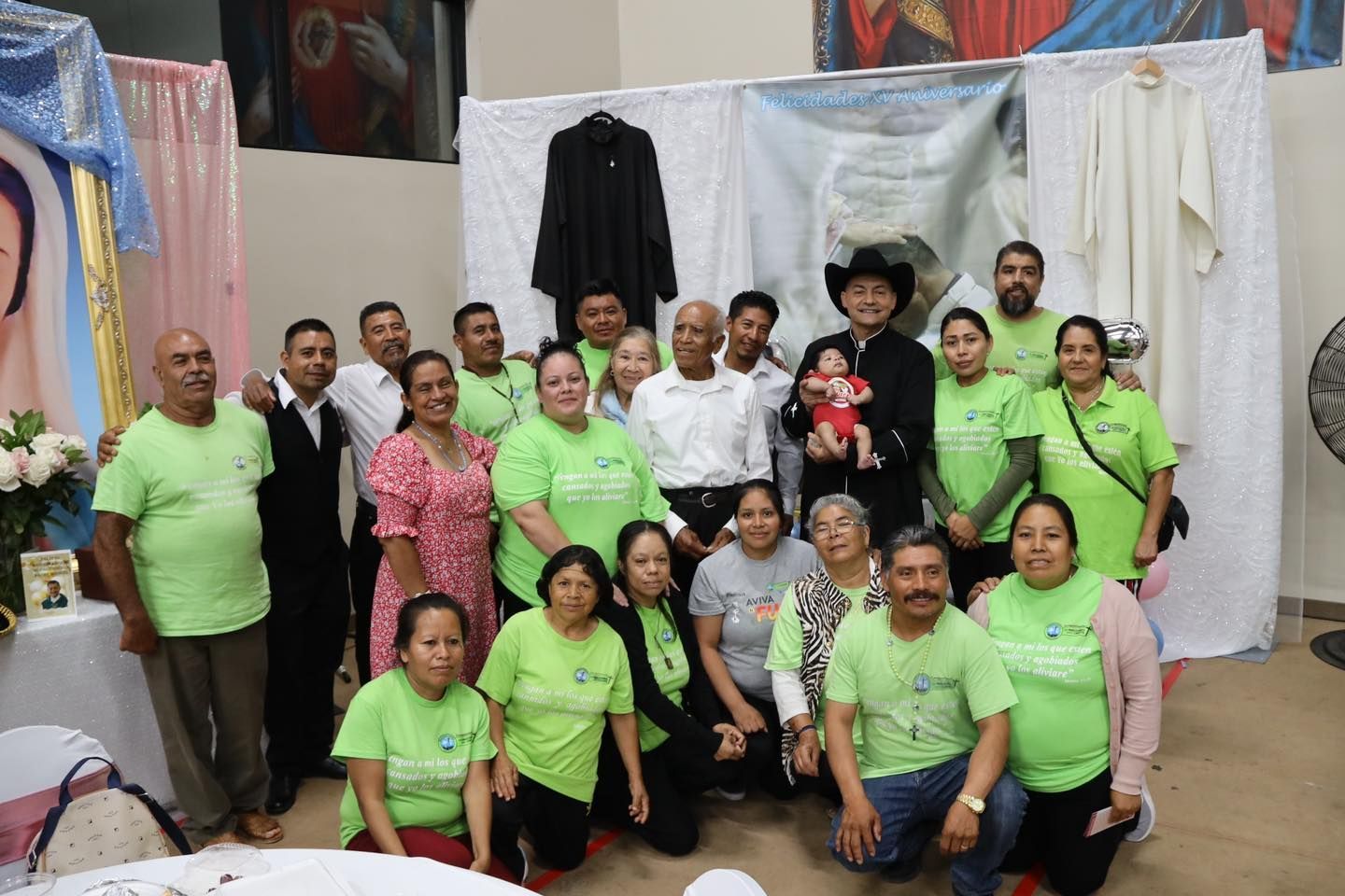 Group photo of people in bright shirts posing indoors with hanging clothes and a child in the center