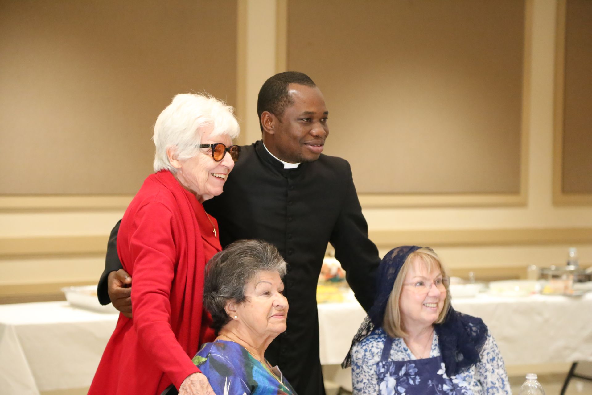 Four people smiling at an indoor event, with two standing behind two seated women.