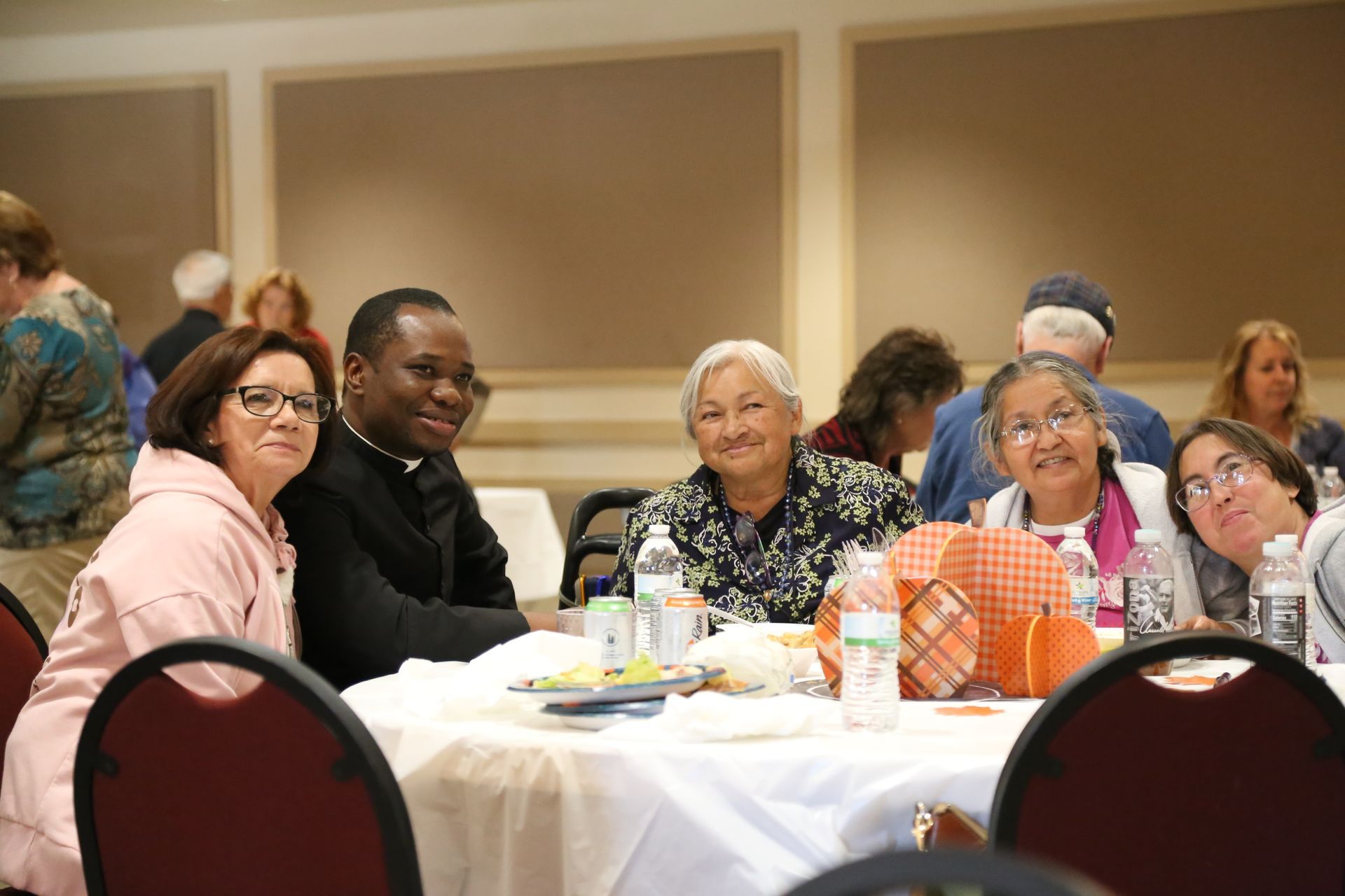 People seated at a round banquet table in a conference room, smiling toward the camera.