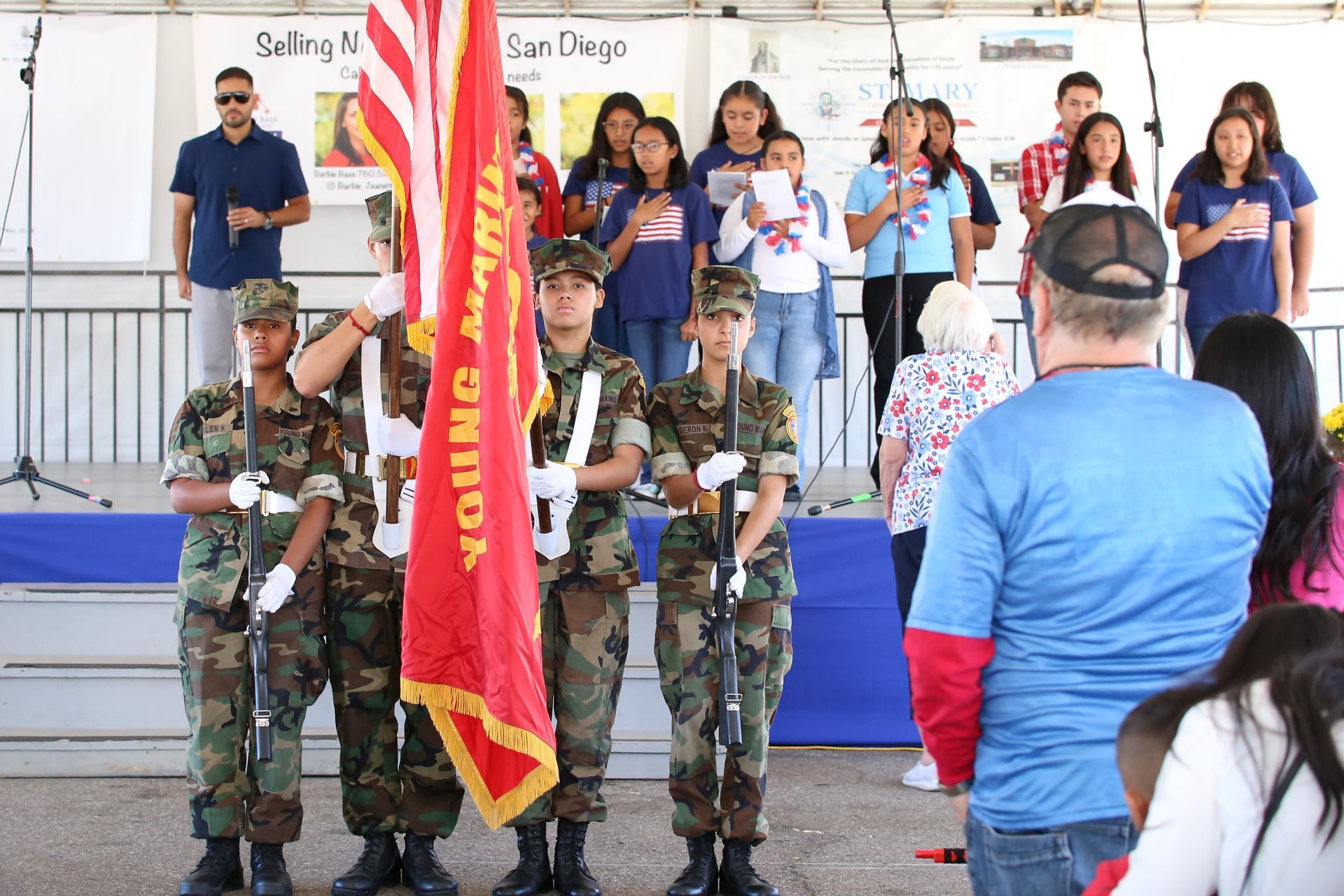 Uniformed honor guard holding flag at ceremony stage with audience in background