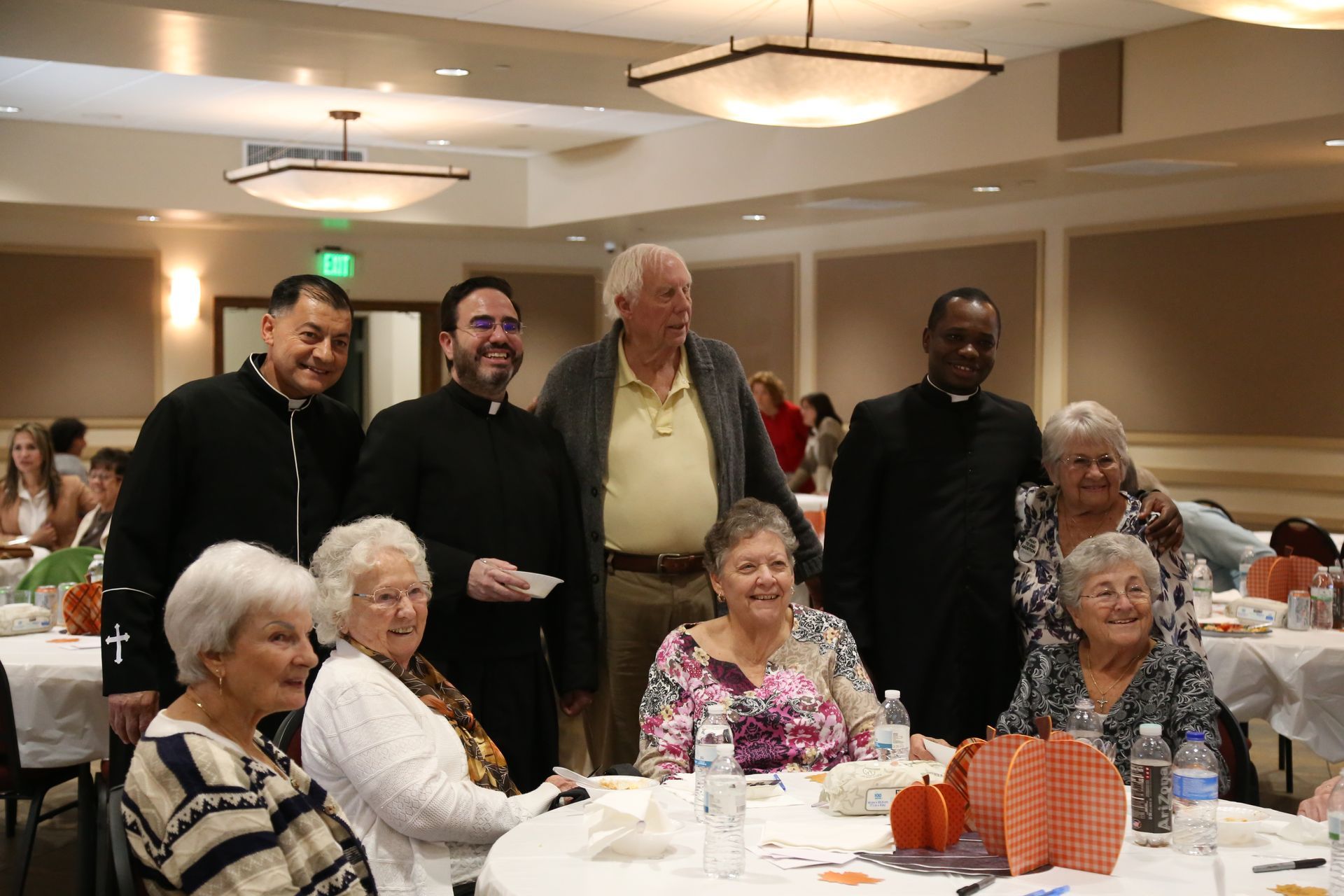 People gathered at a banquet table in a warmly lit dining hall, posing and smiling.