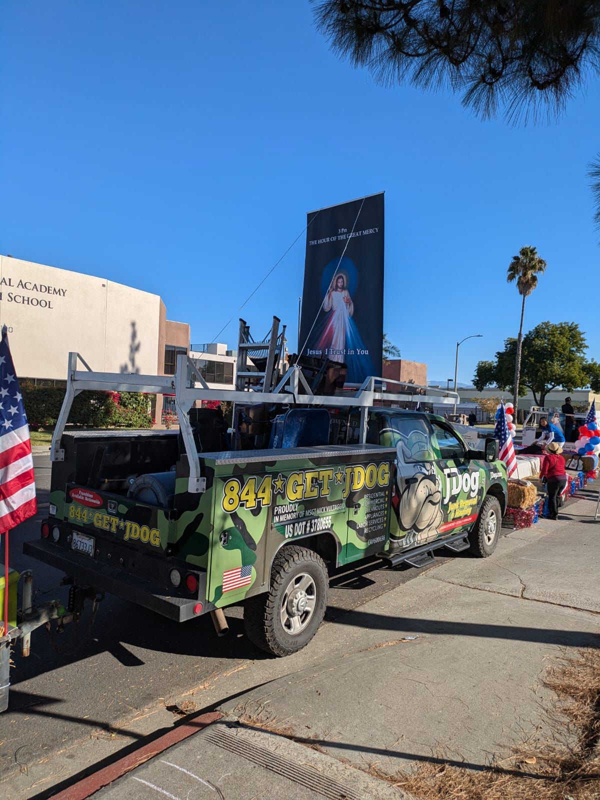Decorated car parked in a sunny street parade, with American flags and people nearby.