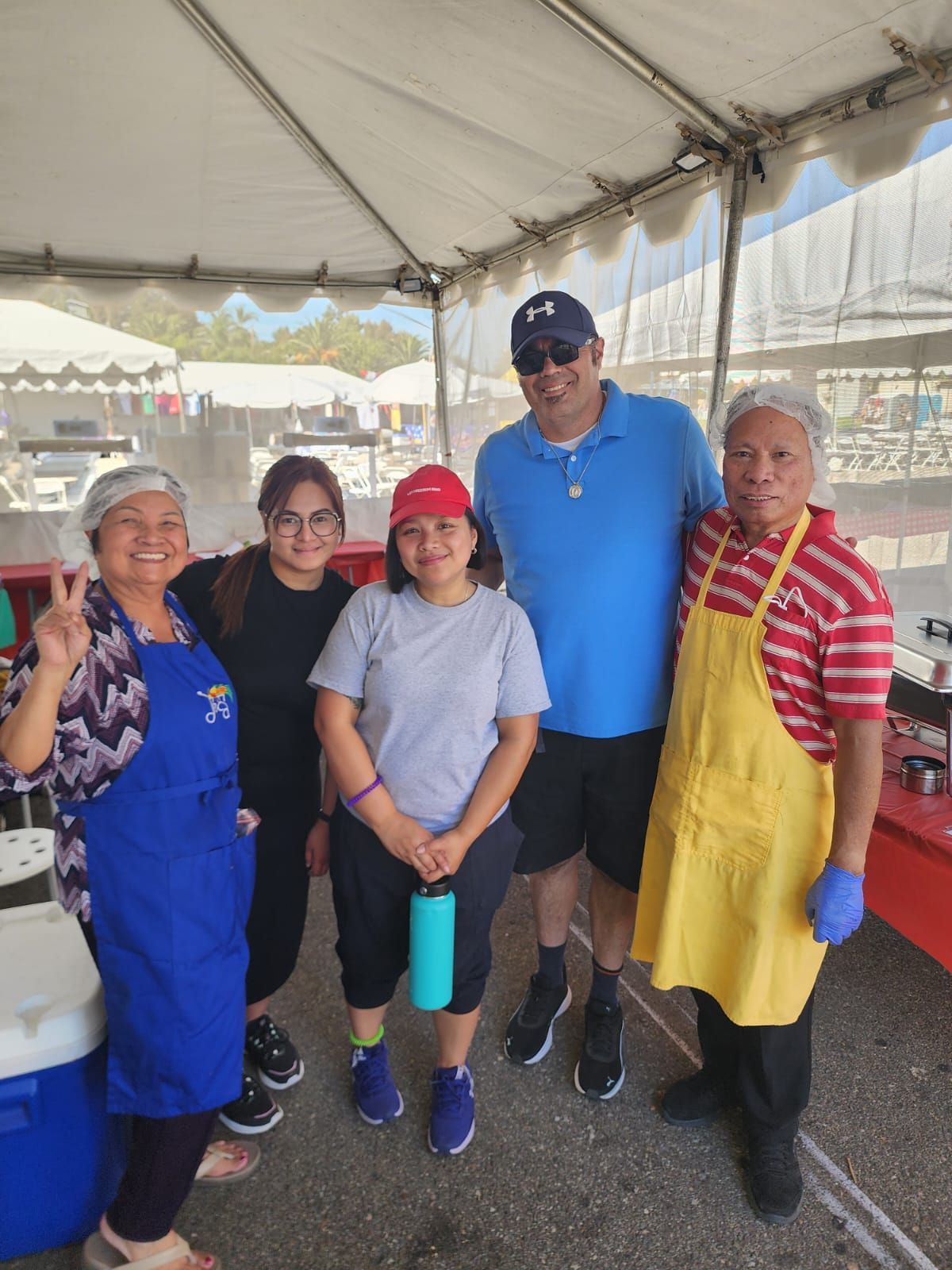 Five people posing under a white event tent, with food tables in the background.