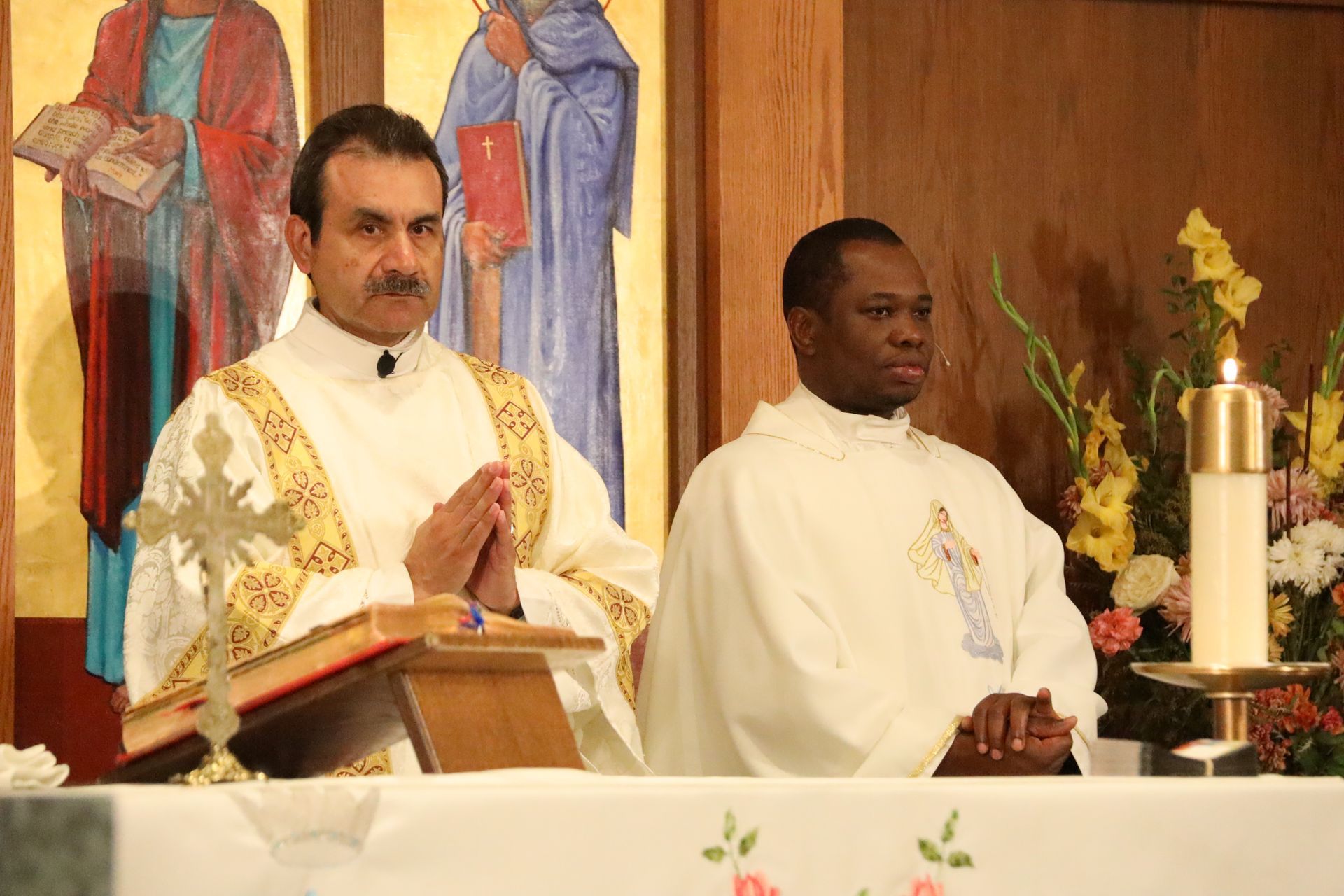 Two clergy members standing at an altar during a church service, one praying with hands together