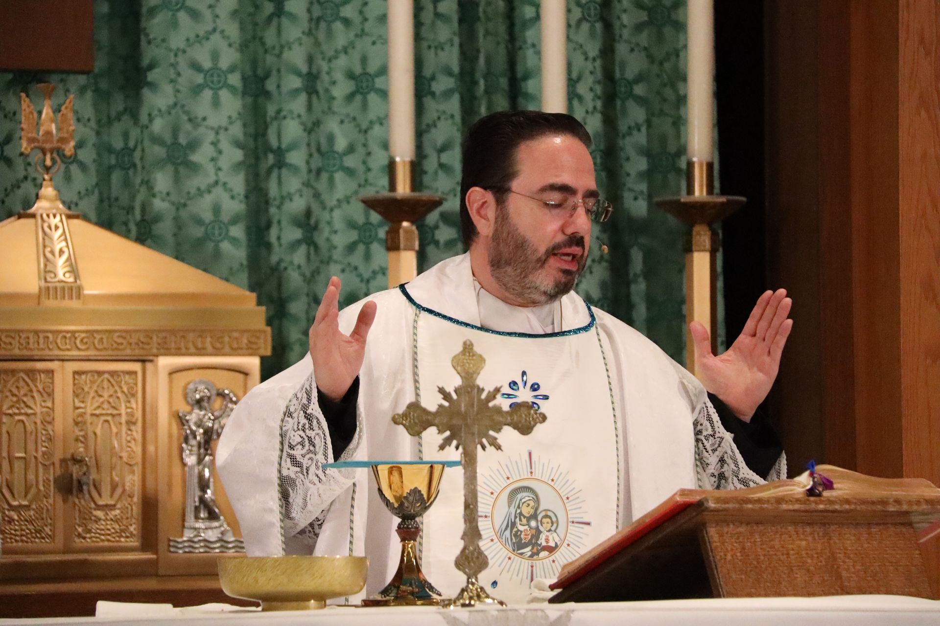 Priest in white vestments with raised hands at an altar during Mass