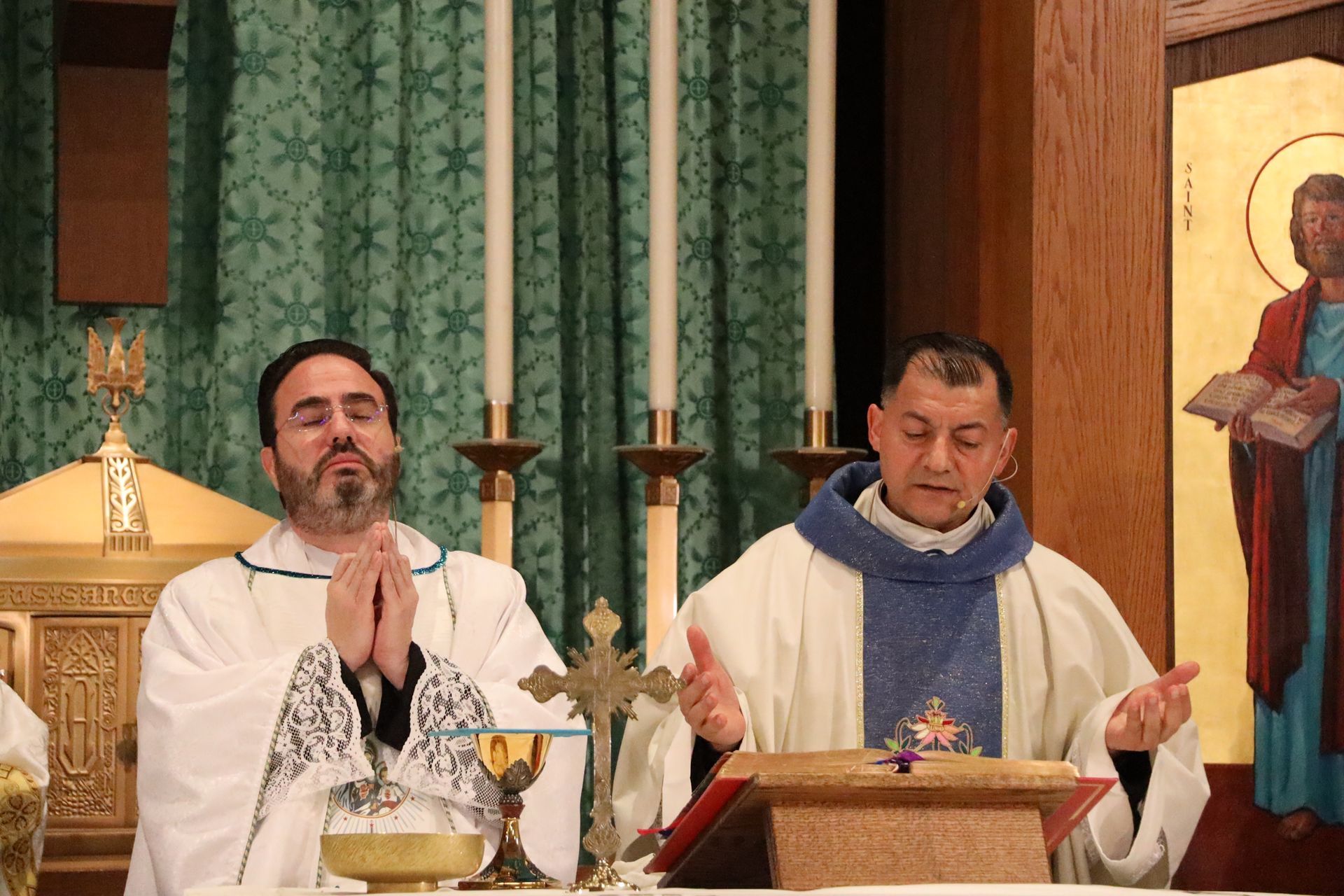 Two priests in white and blue vestments stand at an altar during a church service.