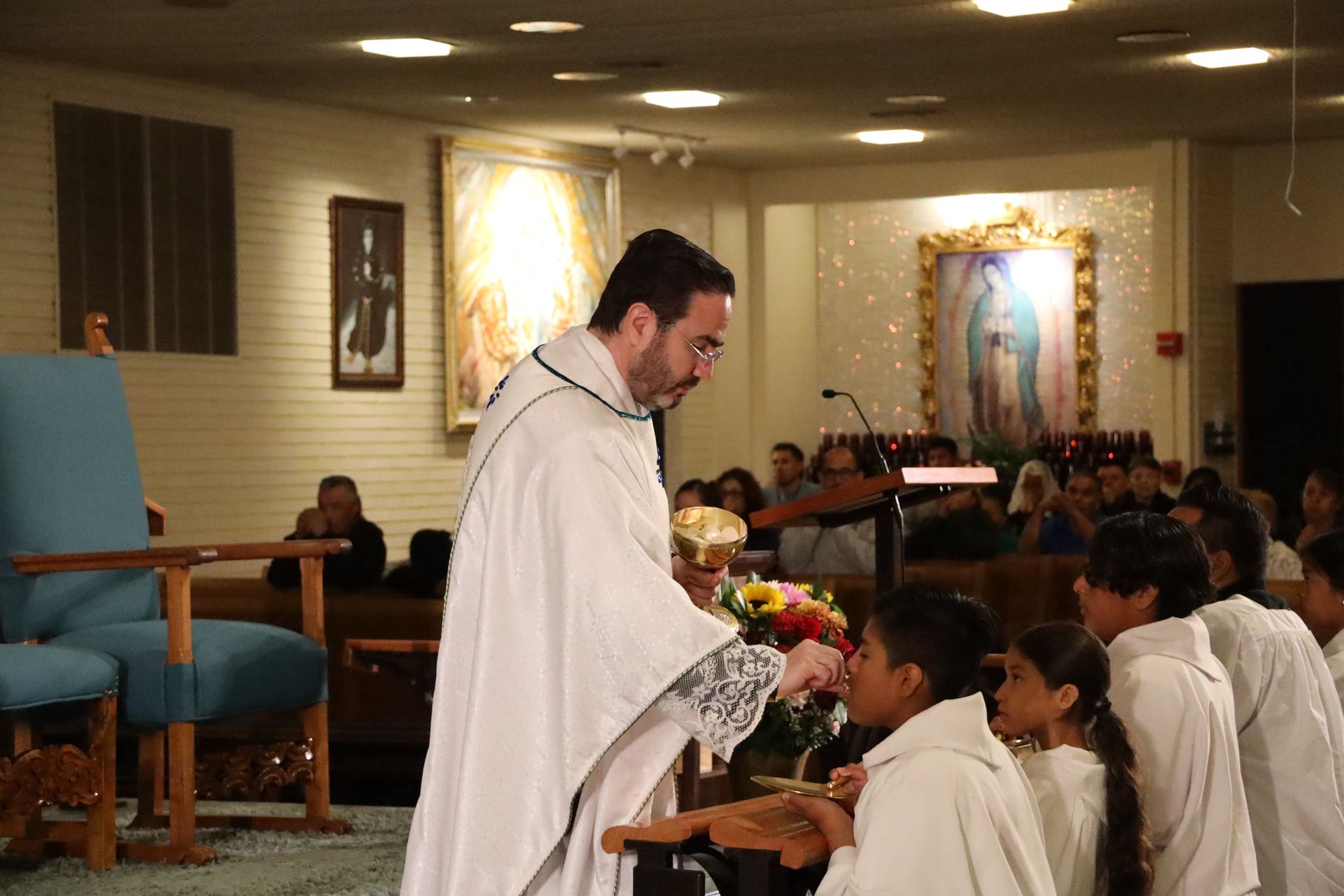 Priest giving communion to kneeling children in a church chapel