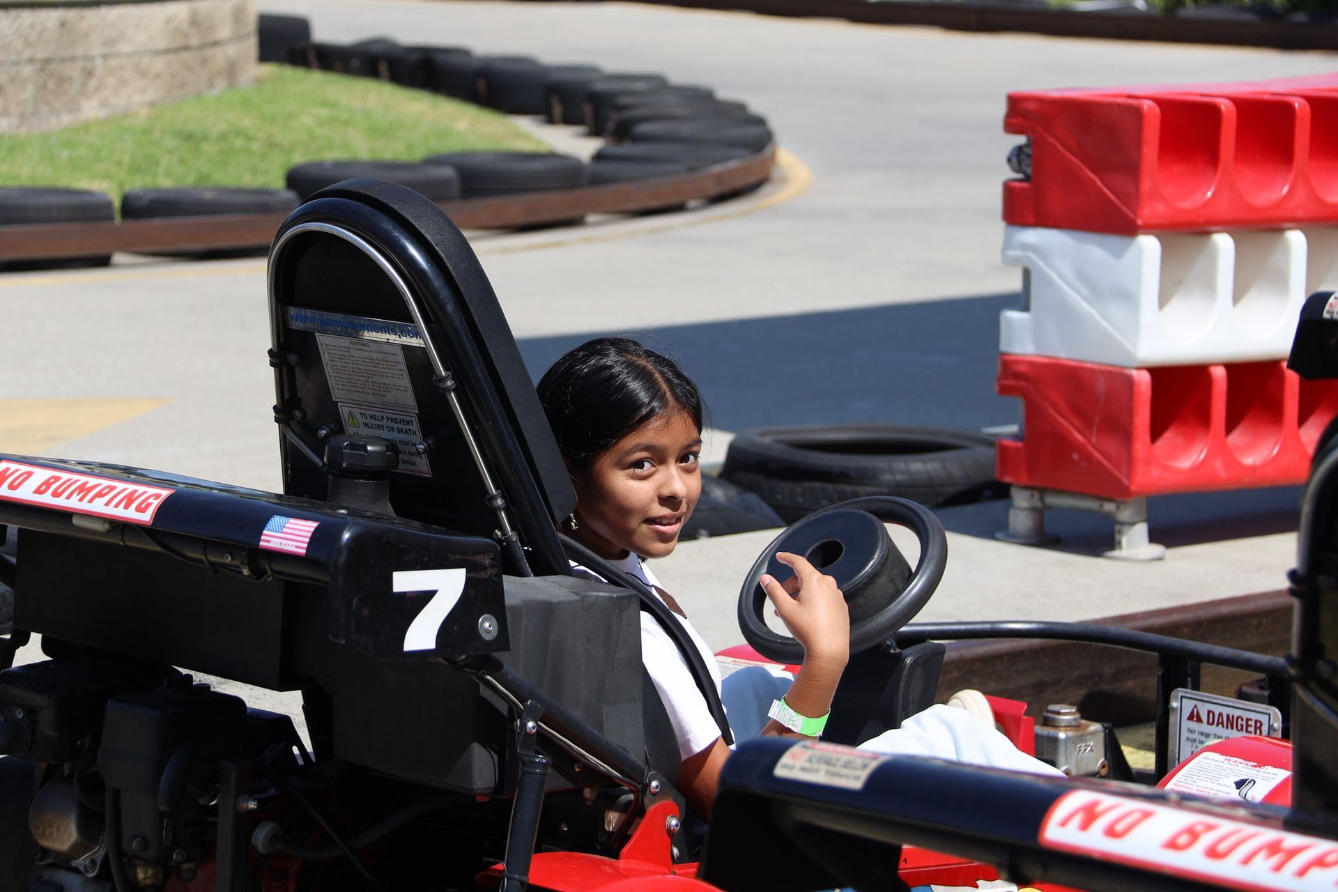 Person driving a black go-kart with number 7 on an outdoor track, smiling at the camera