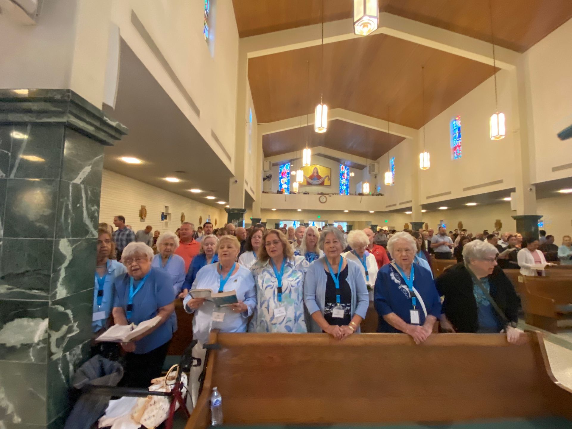 Congregation seated in a church pew, many wearing blue shirts, facing the front during a service.