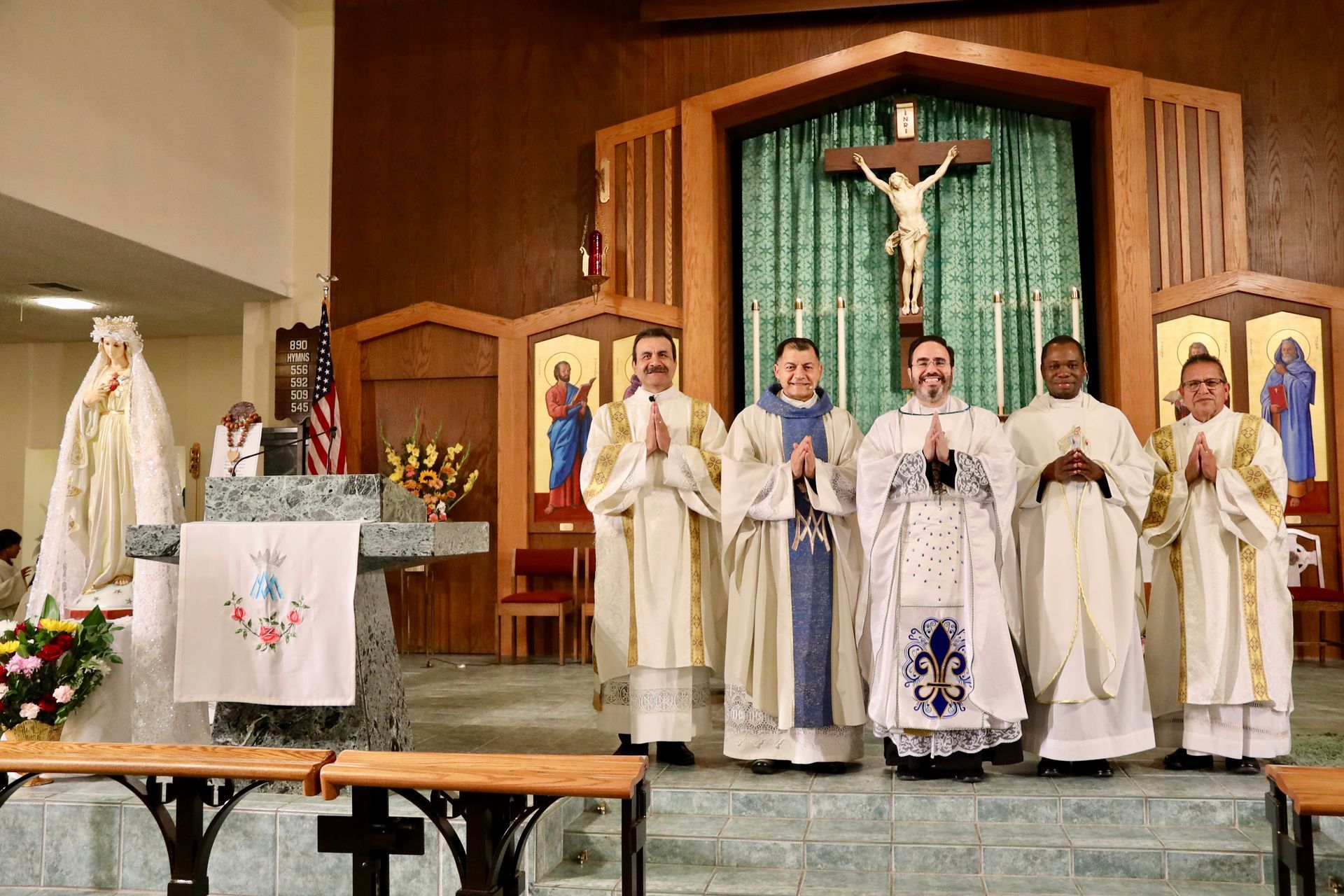 Priests standing at a church altar during Mass, with a crucifix and candles behind them.