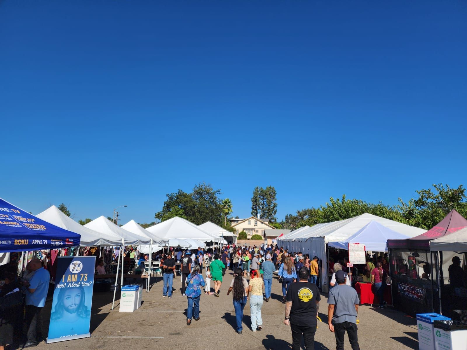 Outdoor market with white tents and people walking under a bright blue sky