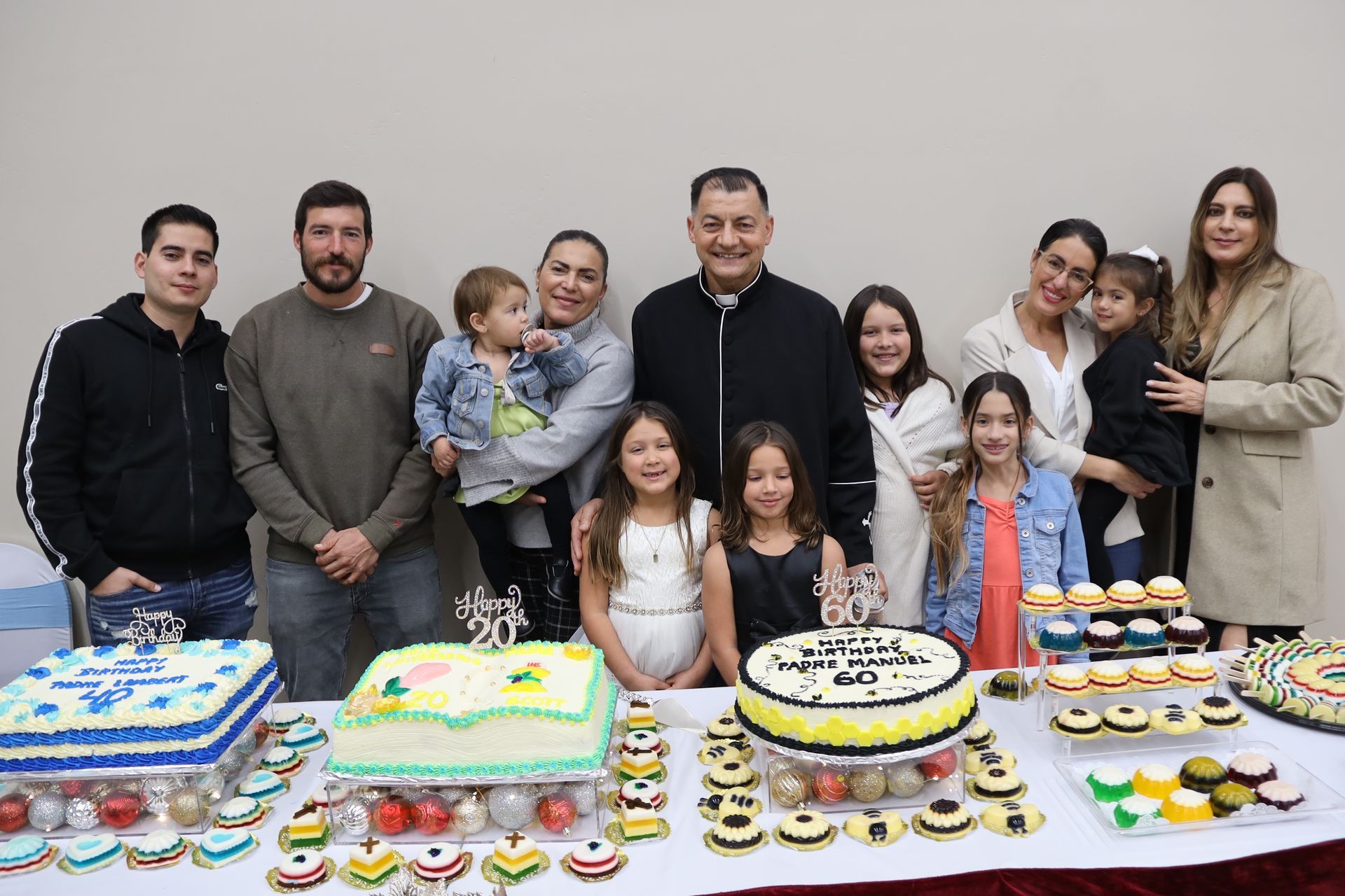 Group gathered behind a table of decorated cakes and cupcakes, posing for a celebration photo.