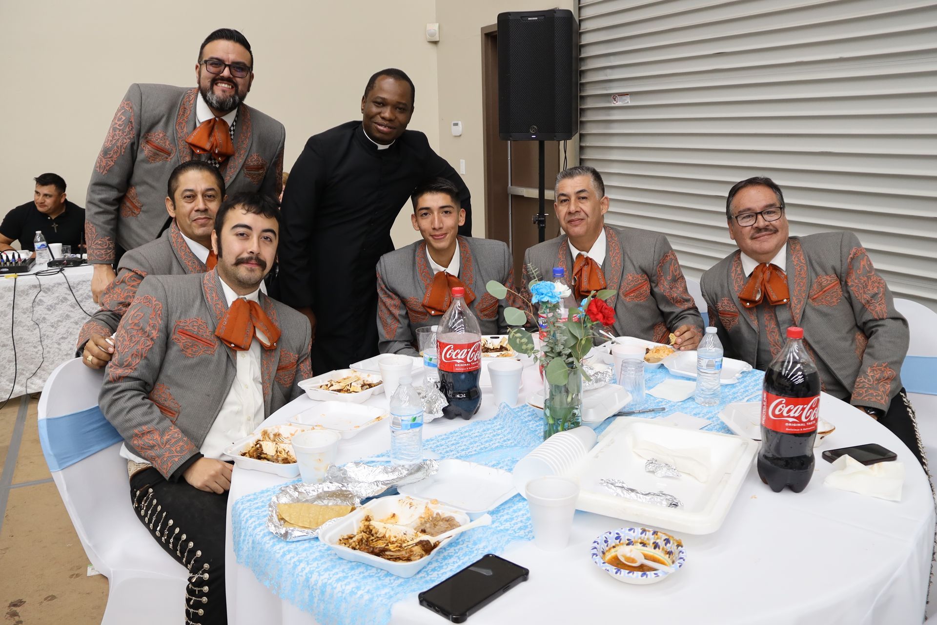Group of people seated at a banquet table, smiling in gray suits with orange bow ties.