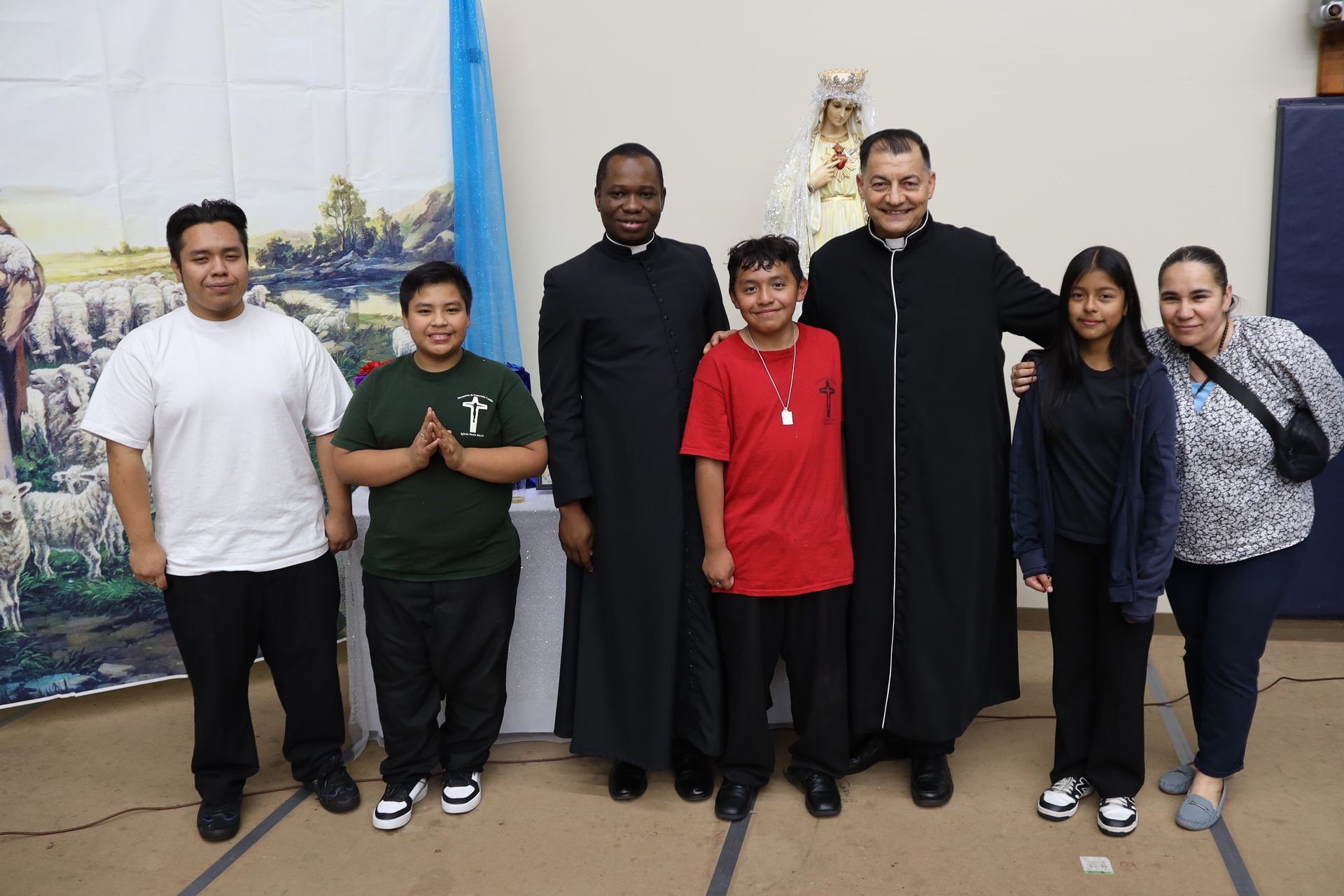 Six people stand indoors with two priests, posing for a group photo.