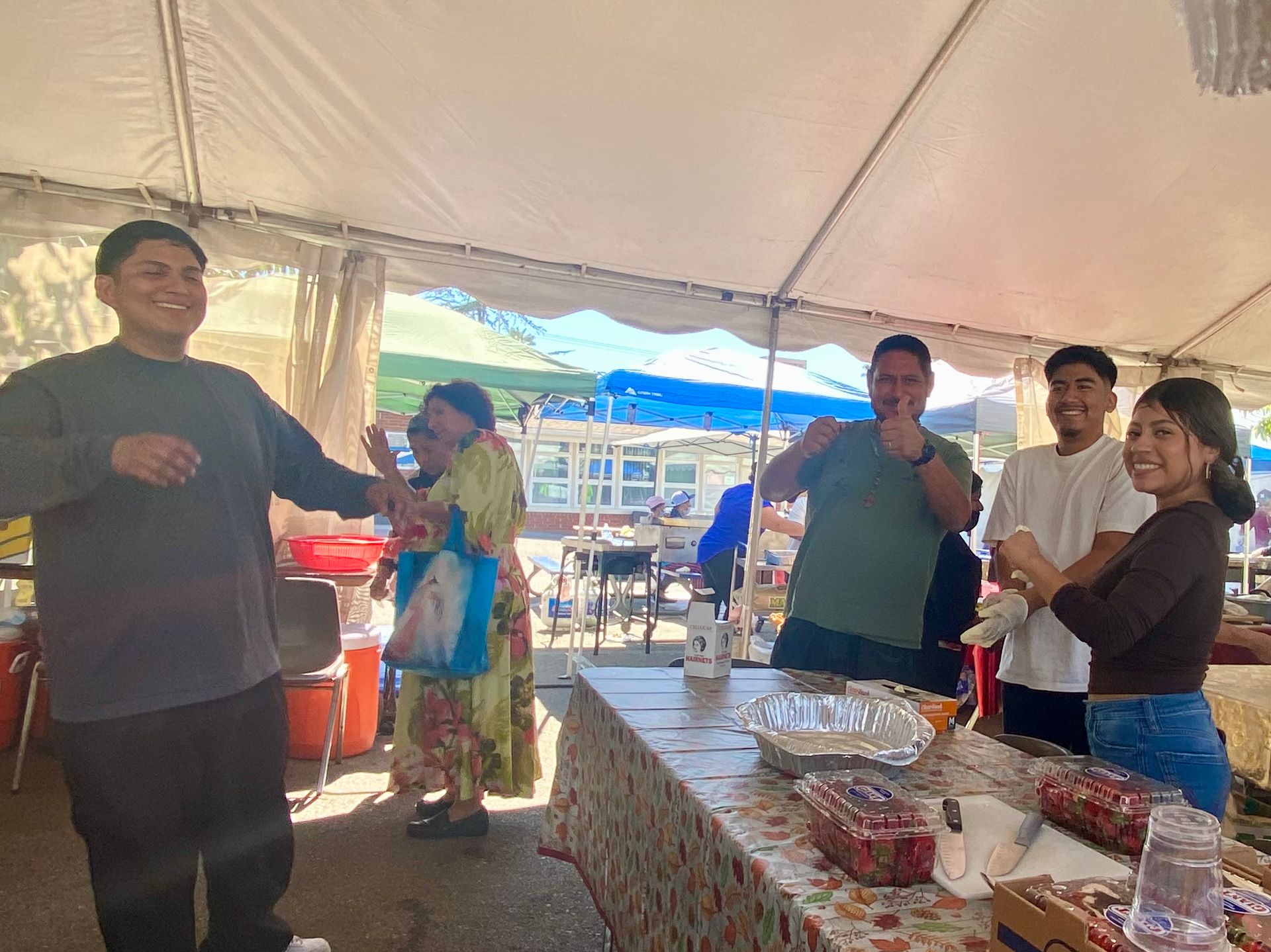 People standing at a food table under a white tent at an outdoor gathering