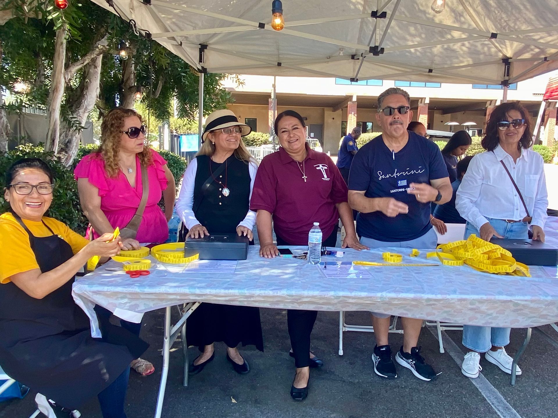 Group seated at a long table under a canopy, smiling at an outdoor event with yellow decorations.