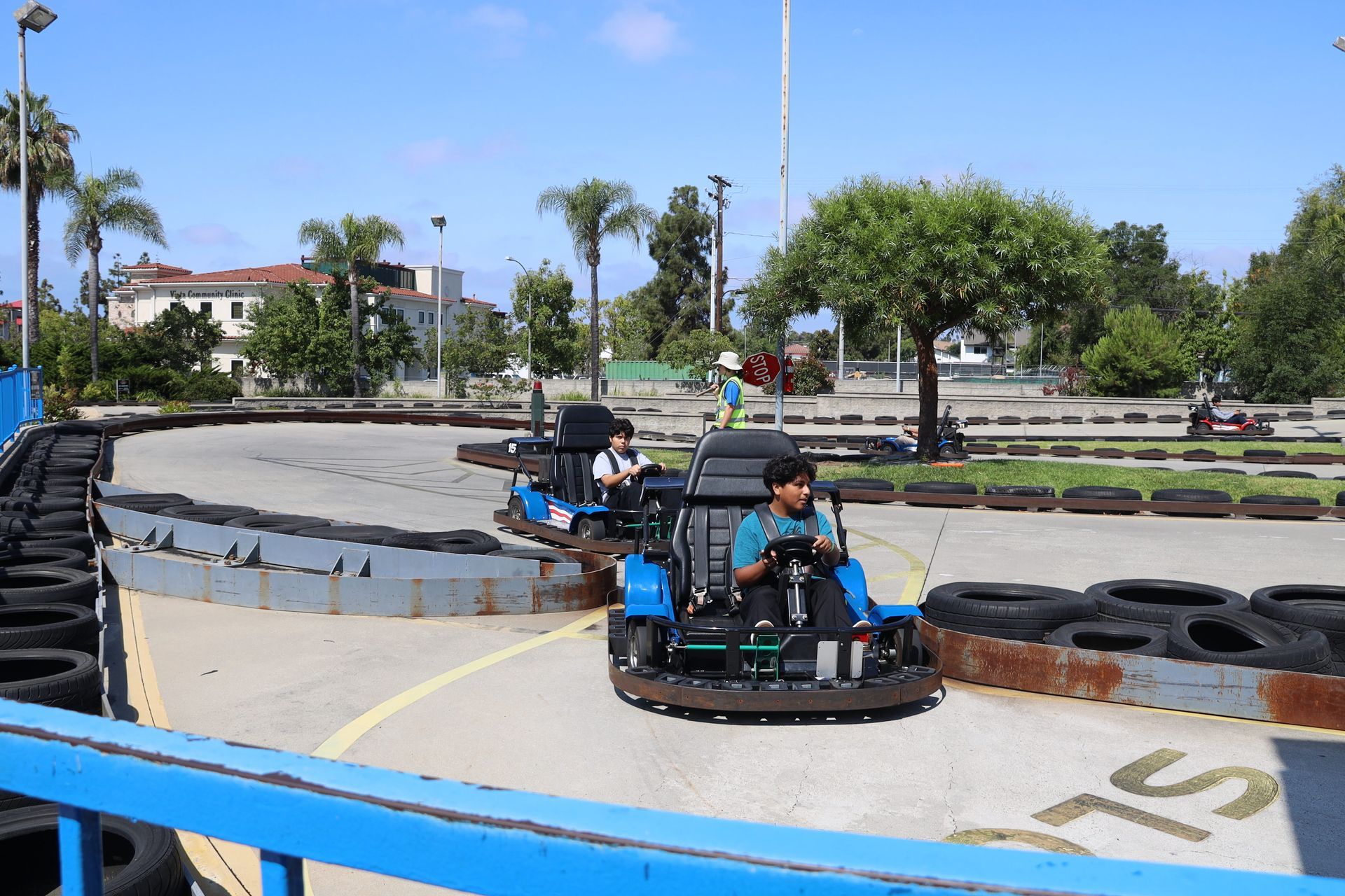 People driving bumper cars on a sunny outdoor track, with tires and trees in the background