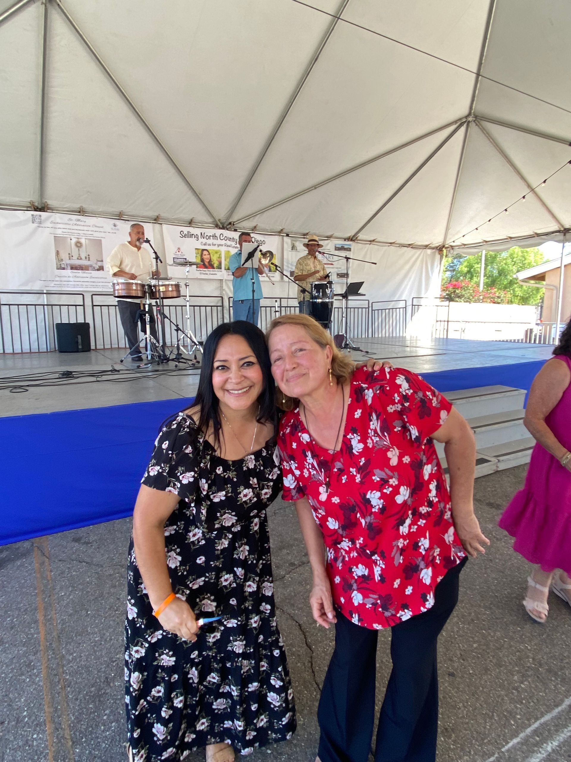 Two people smiling and posing under a tent in front of a stage with musicians