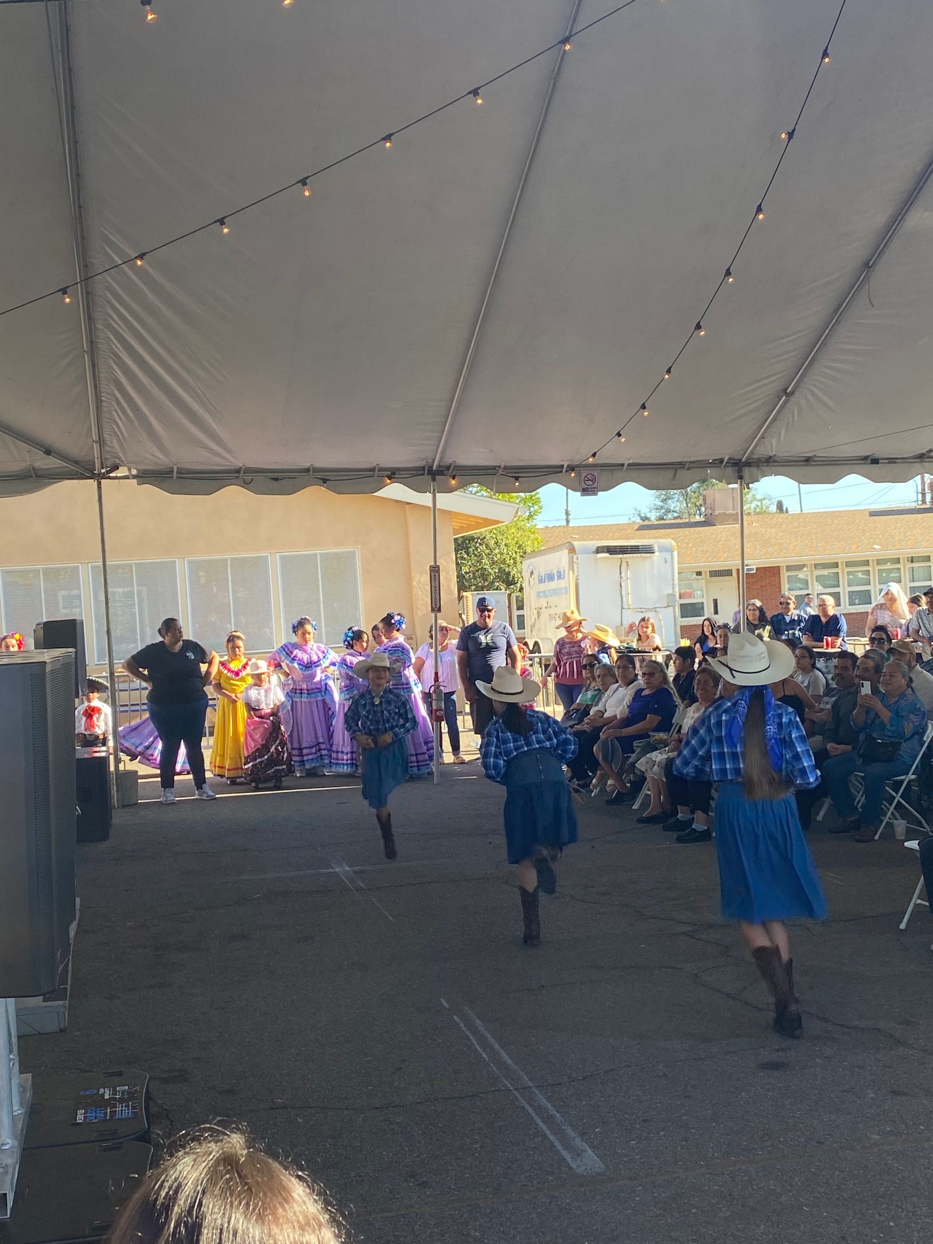 Children in blue uniforms running under a large tent toward a group of people near a stage