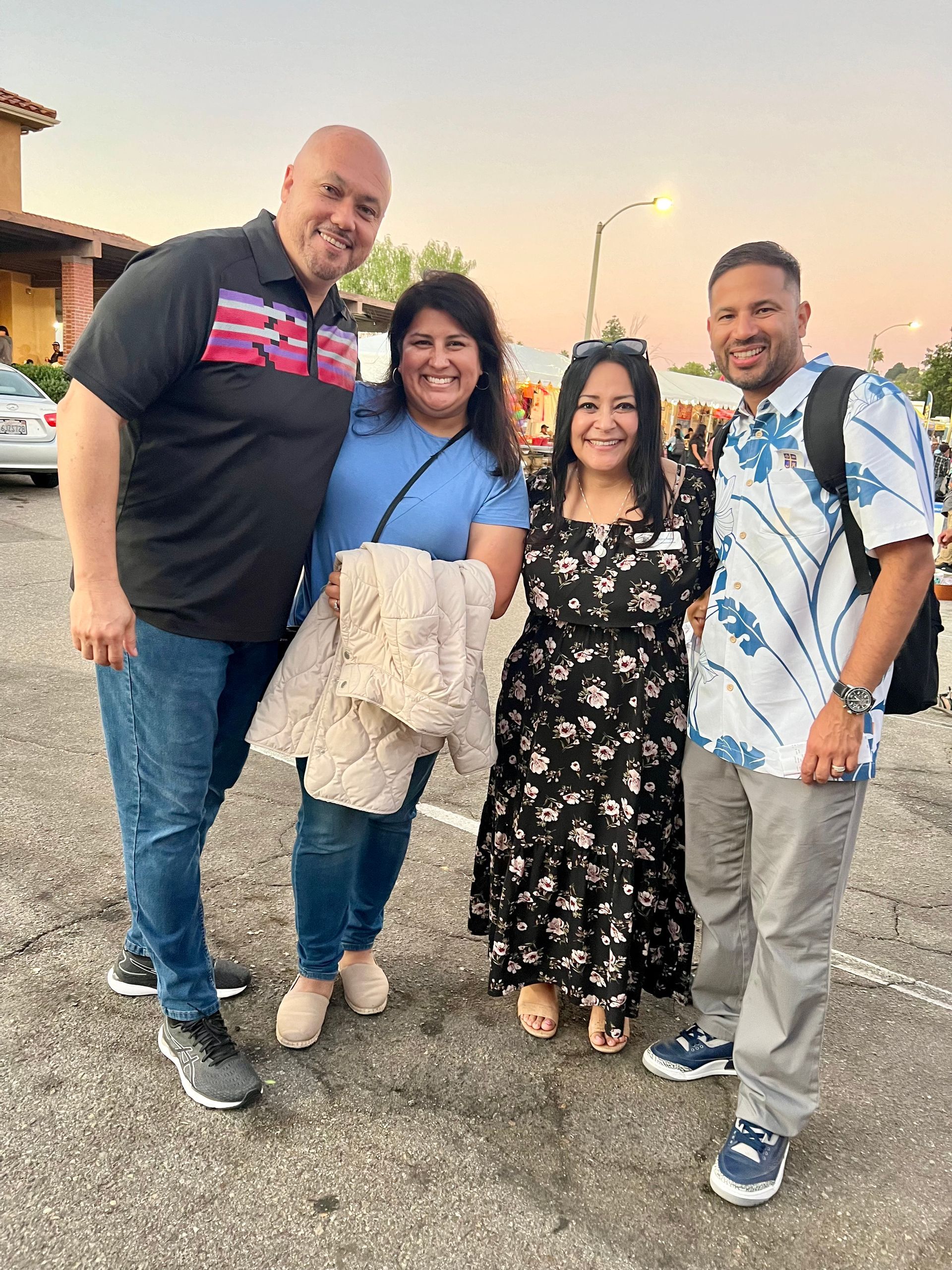 Four people smiling and posing together outdoors at sunset on a roadside.